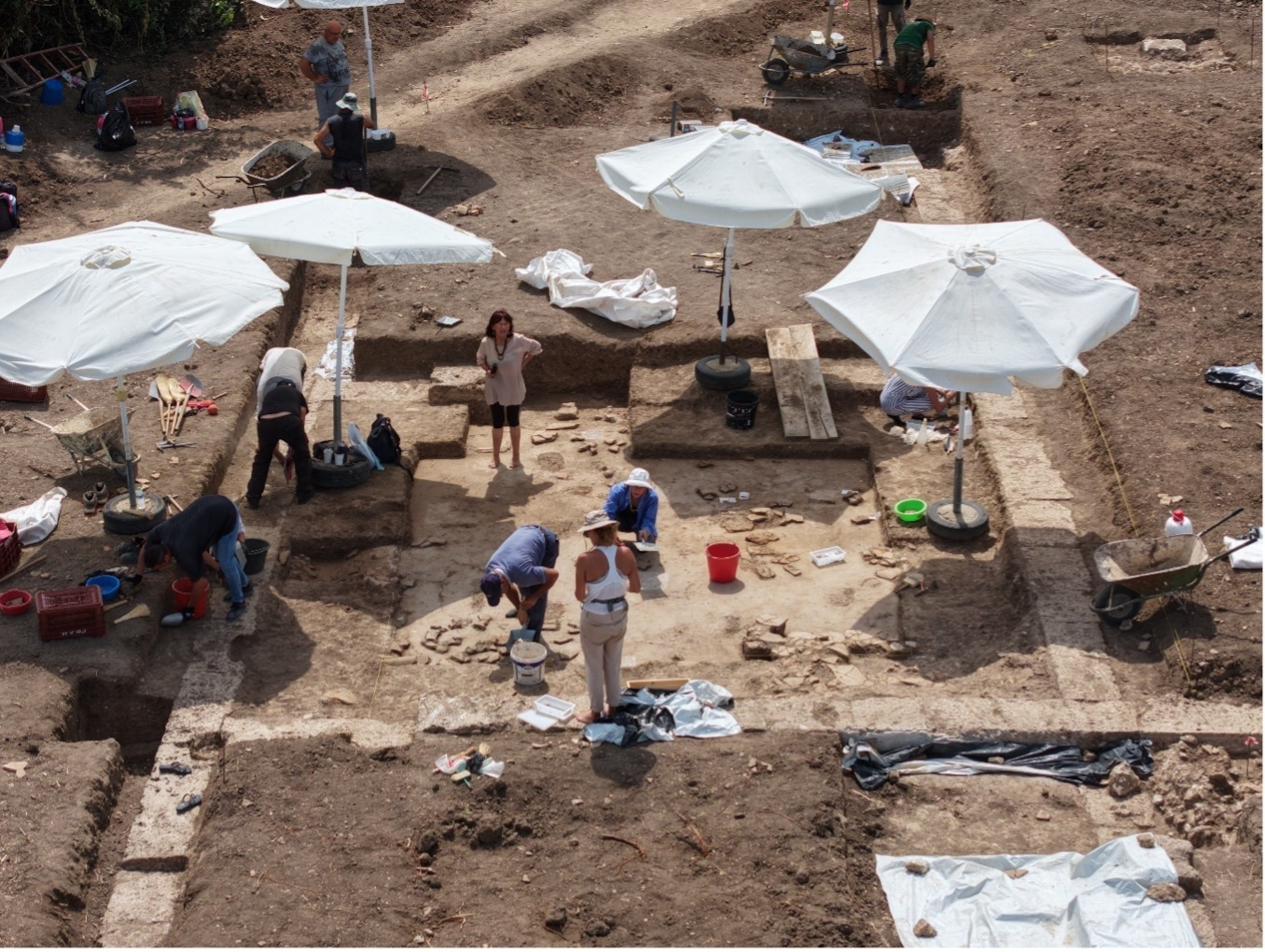 An aerial view of an archaeological excavation reveals the stone foundations and layout of ancient buildings exposed beneath the soil.