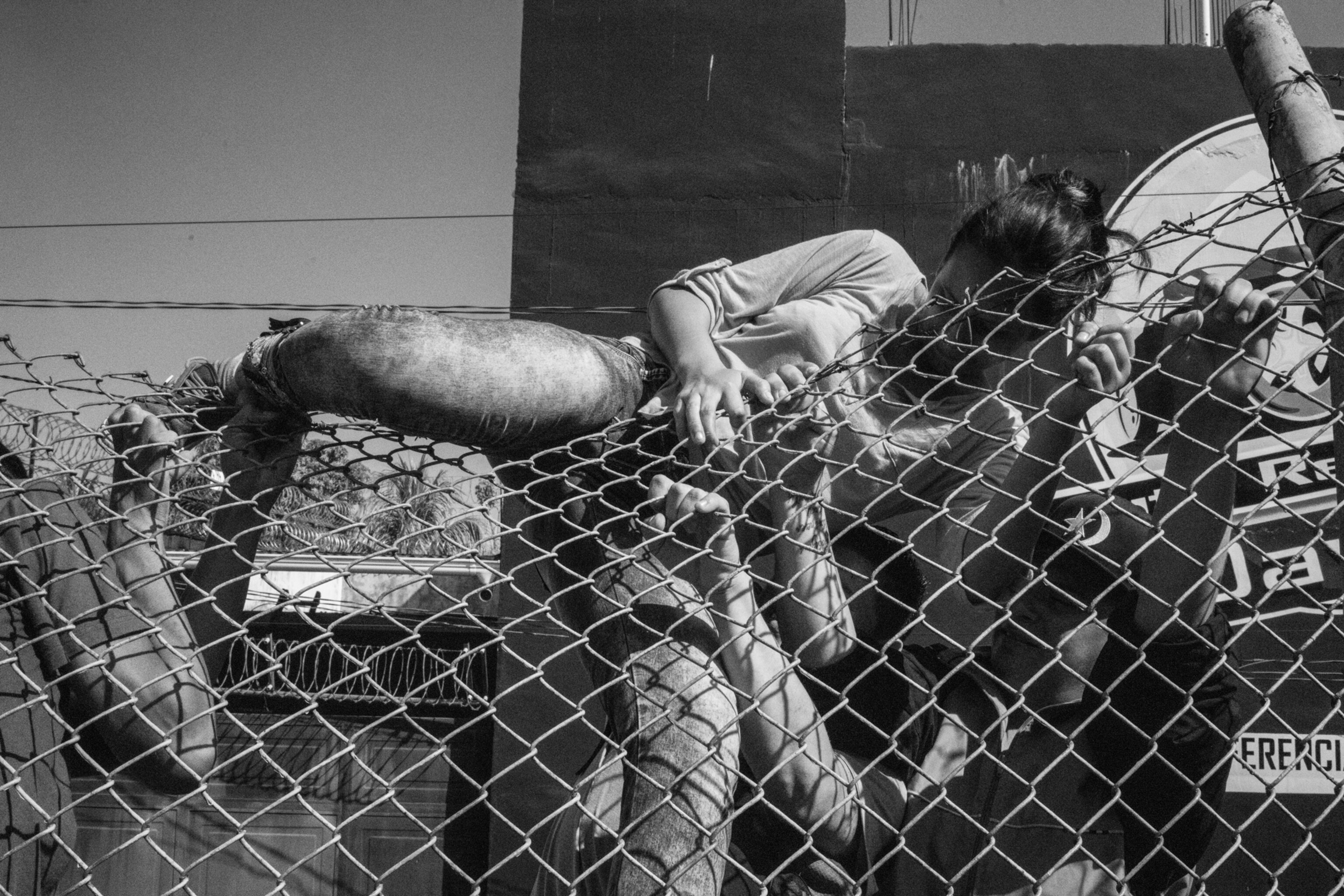 a women climbing over a wire fence with men assisting