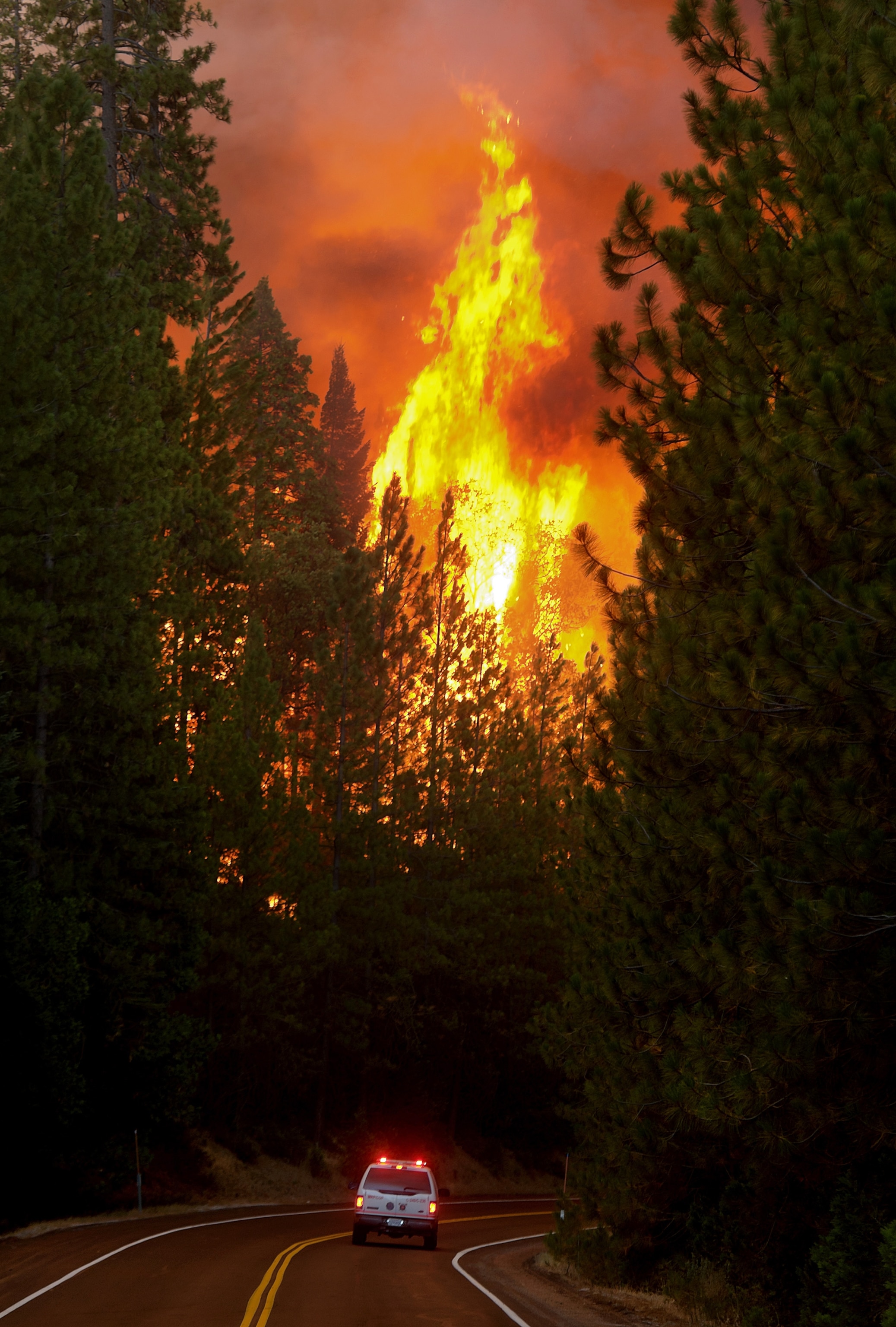 an emergency vehicle driving Highway 120 with flames in the sky during the Rim Fire