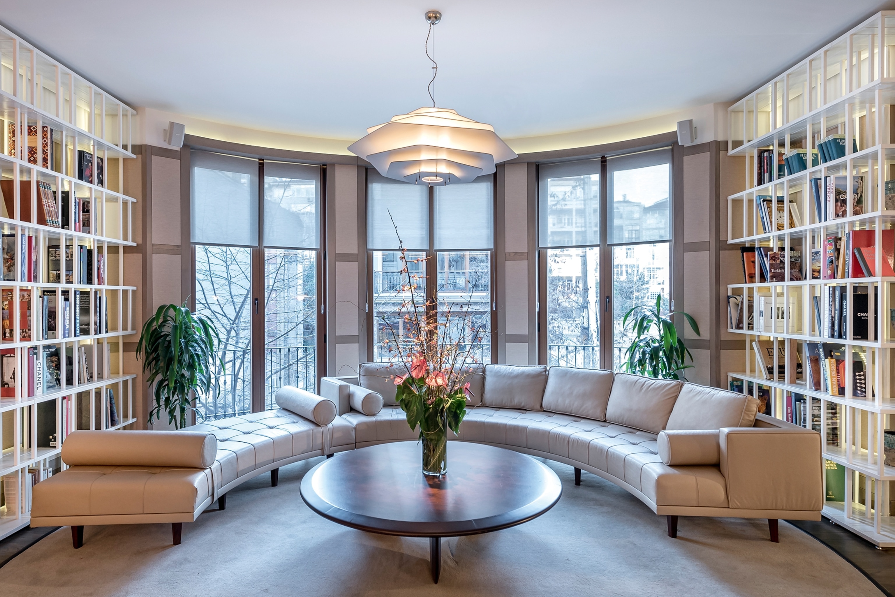 A luxurious rounded window-side lounge with a round able and flowers in a vase.