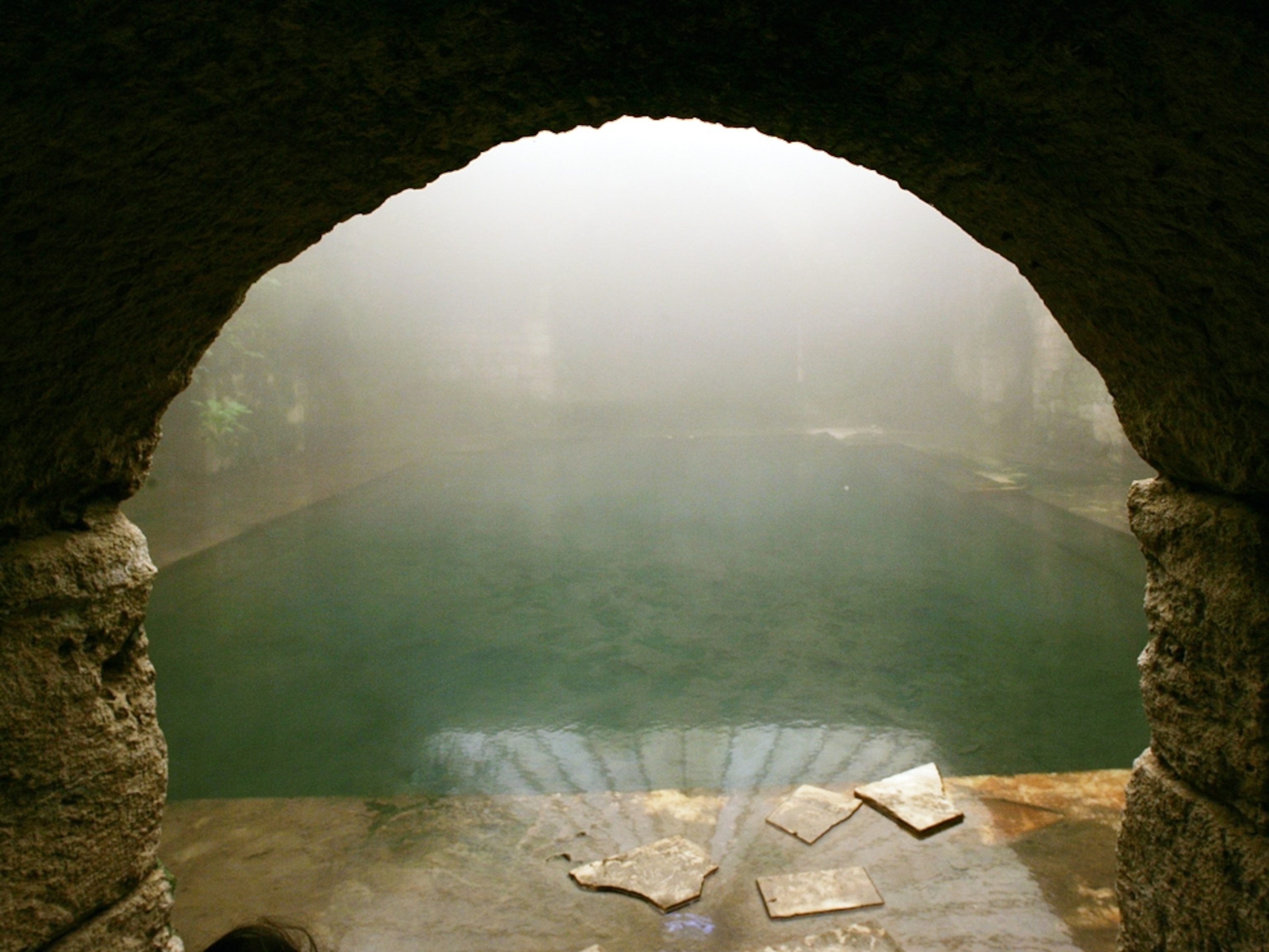 A stone archway frames the thermal pool of an ancient Roman bath.