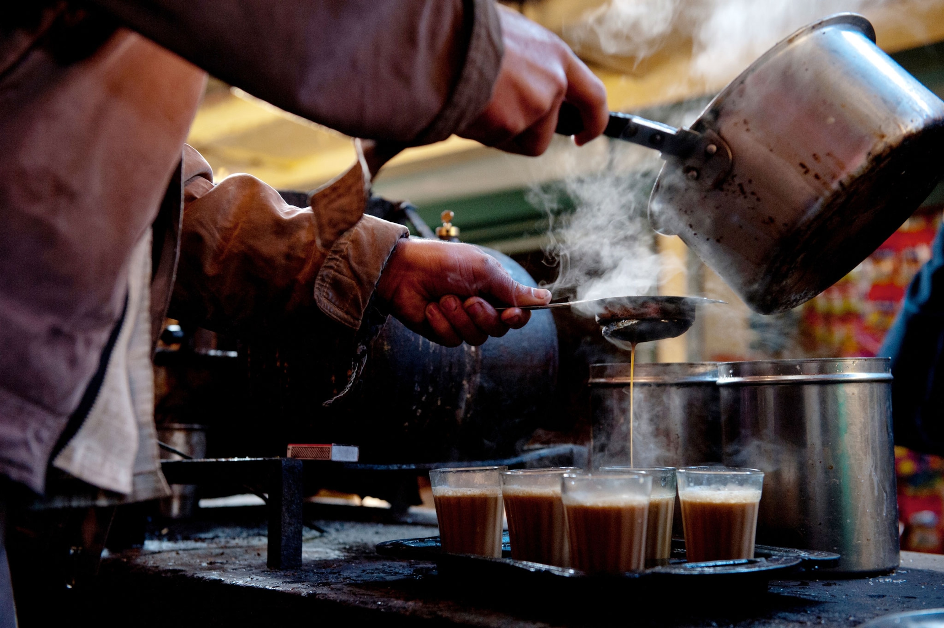 a hands pouring chai into small steaming glasses