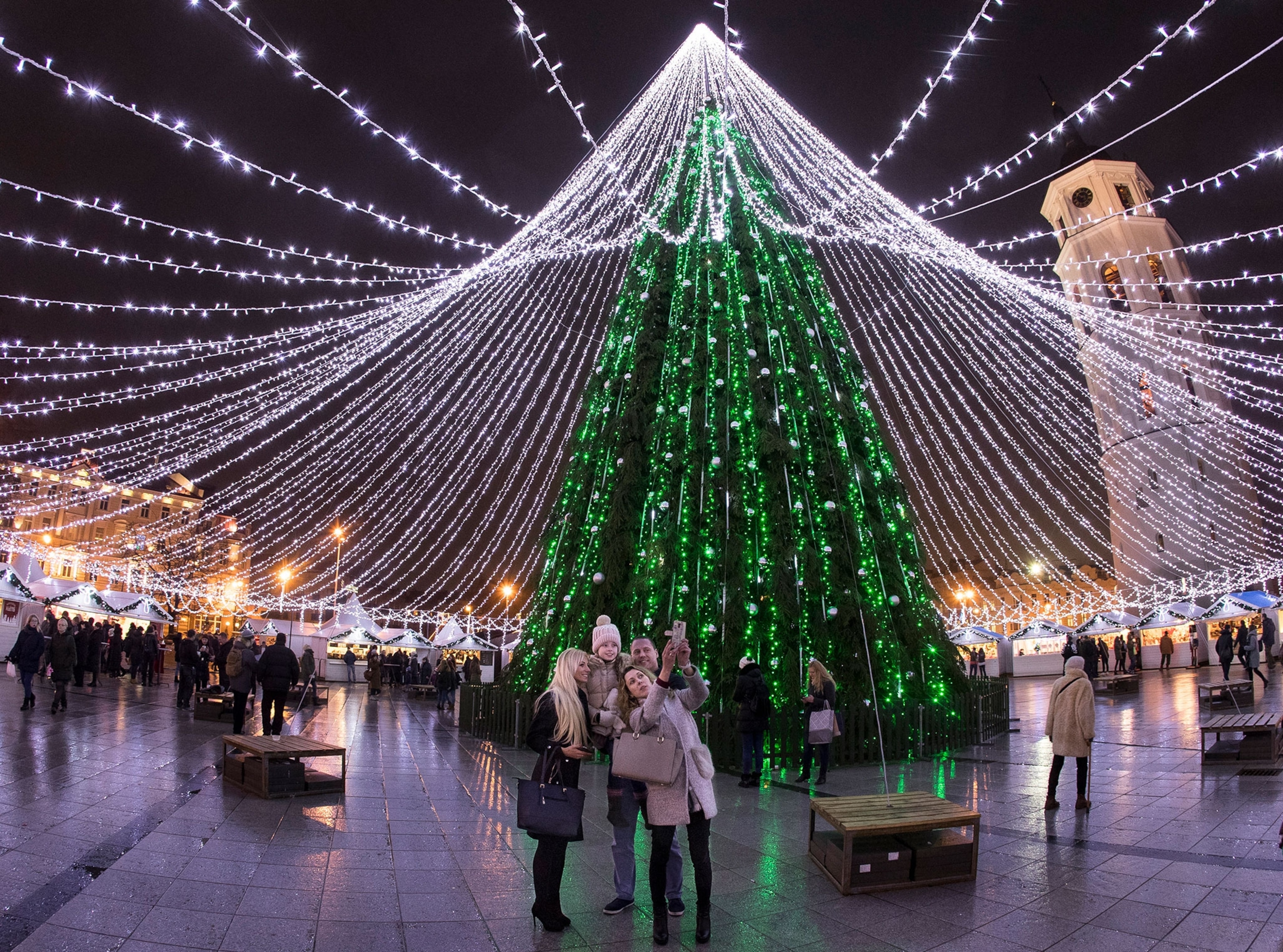 Visitors take a selfie in front of the illuminated Christmas tree at Cathedral square in Vilnius, Lithuania