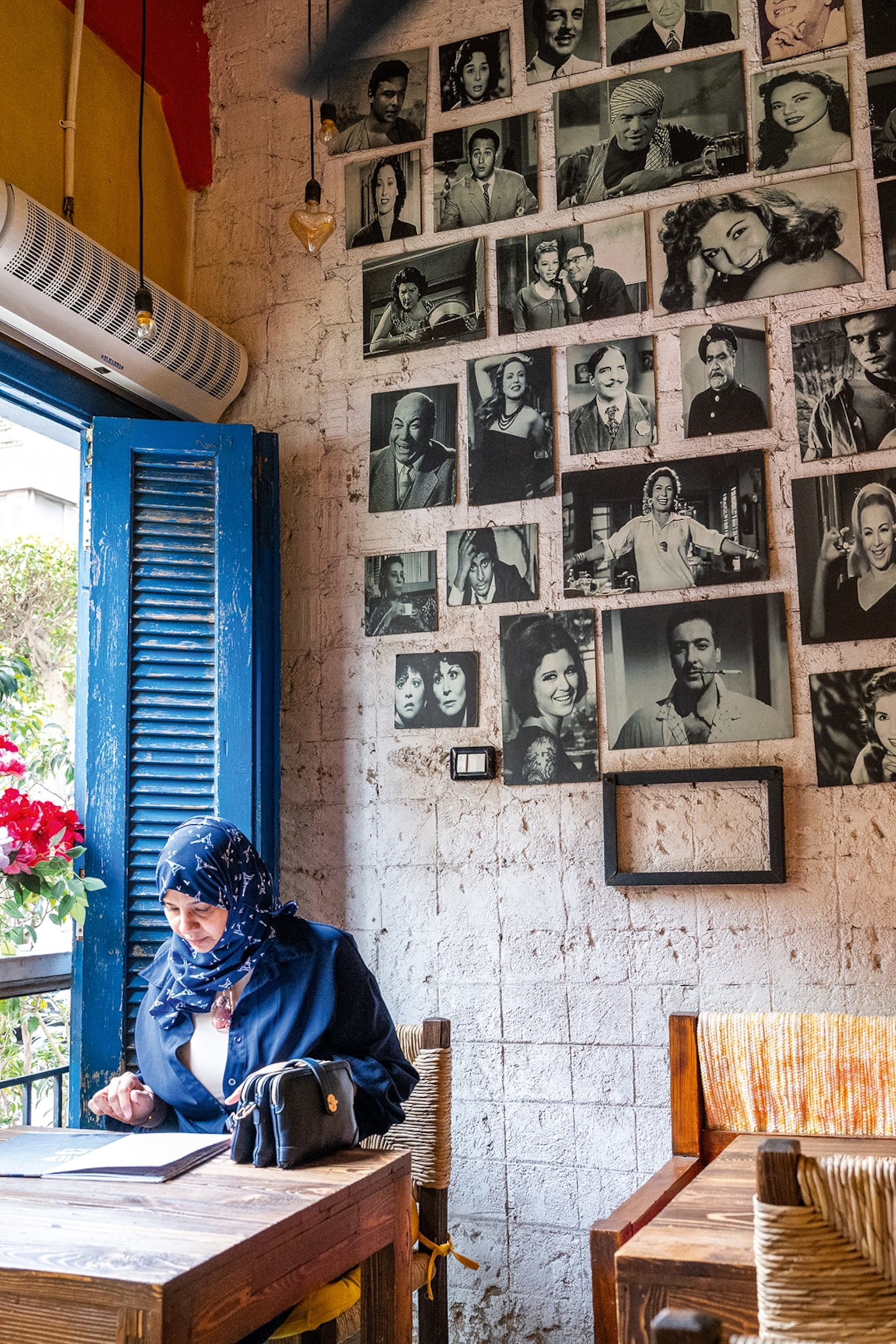 A local woman sitting at the table of a restaurant with framed portraits on the wall behind.