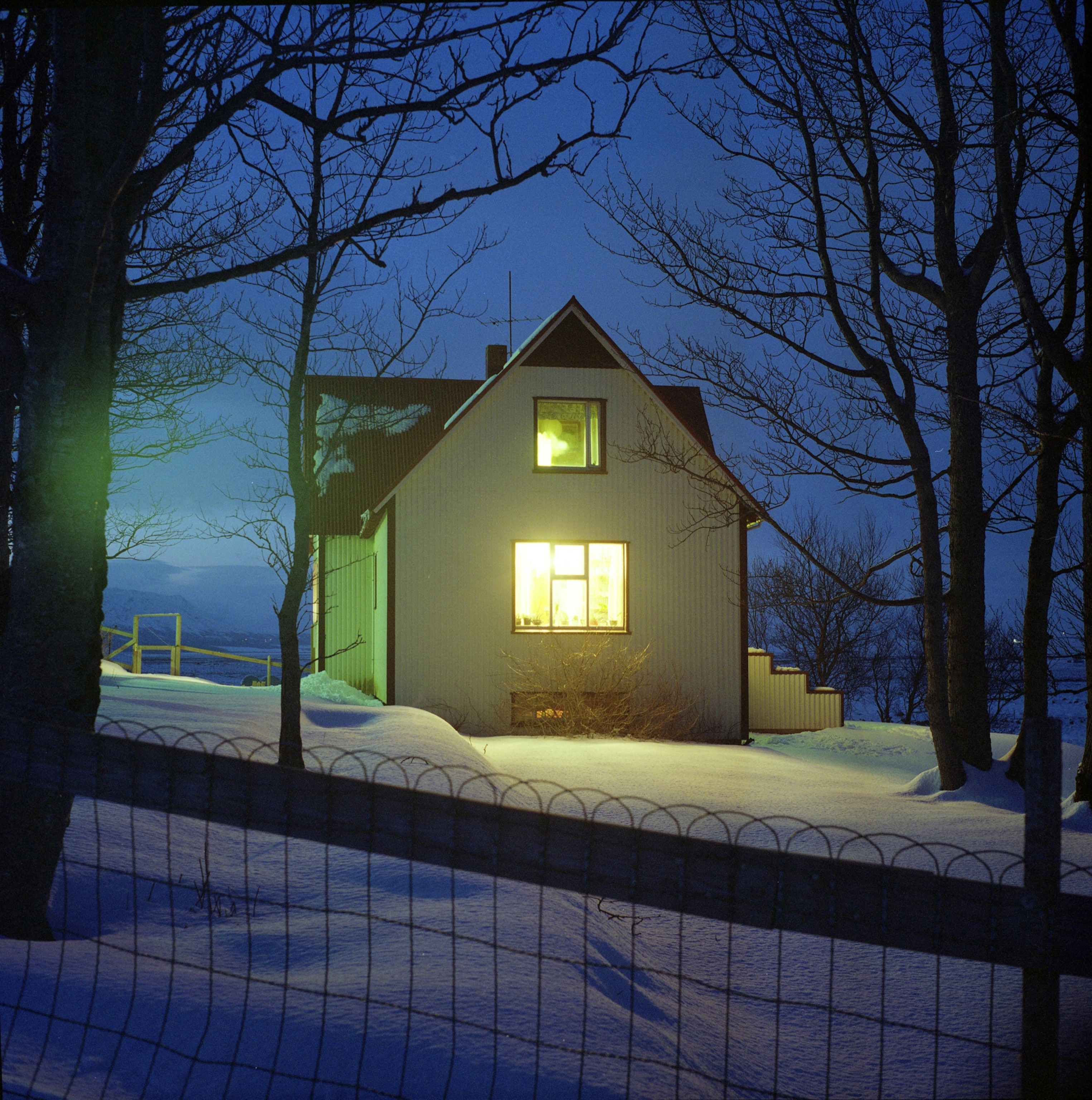 A house with windows aglow at night, snow blanketing the foreground