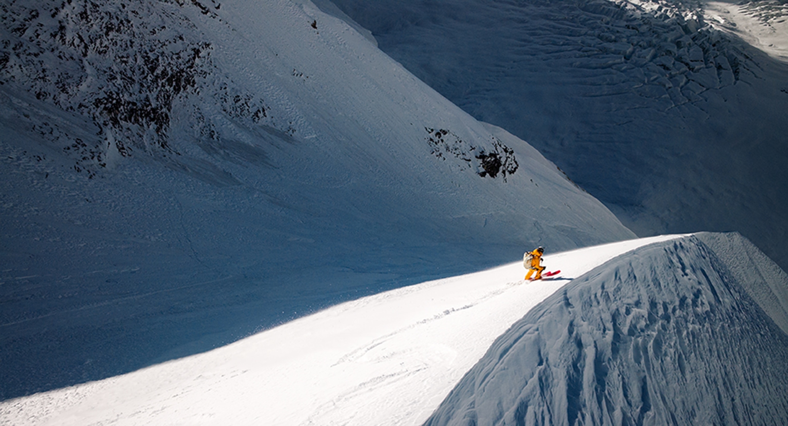 A man skis on a ridge of deep snow with a steep drop-off.