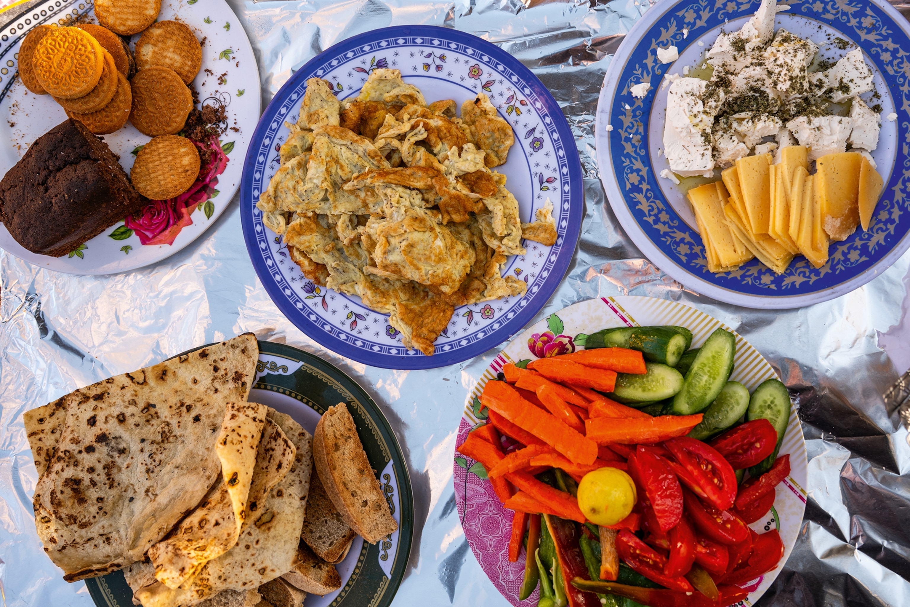 Plates containing eggs, flatbreads, vegetables and feta cheese laid out on foil.