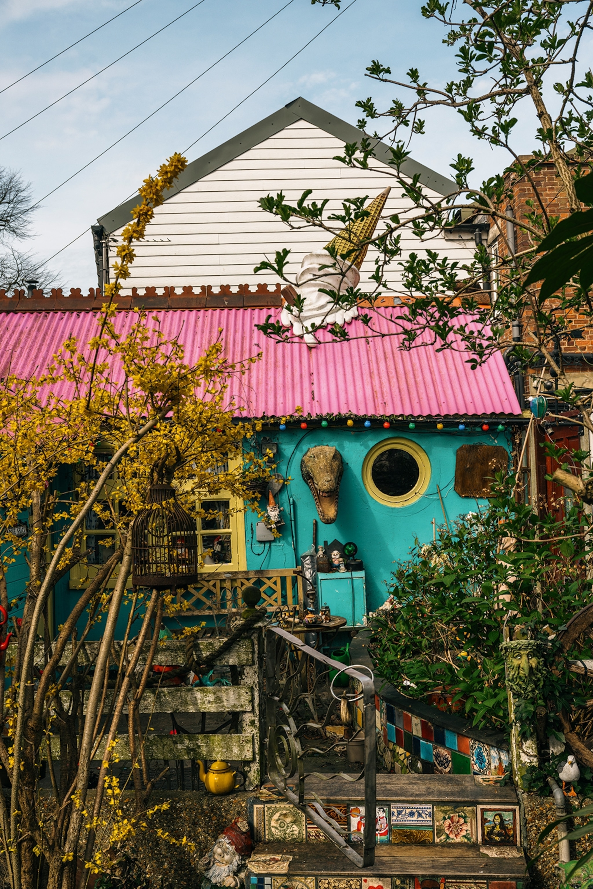 The exterior of a colourful house with gnomes and trinkets in a garden in front.