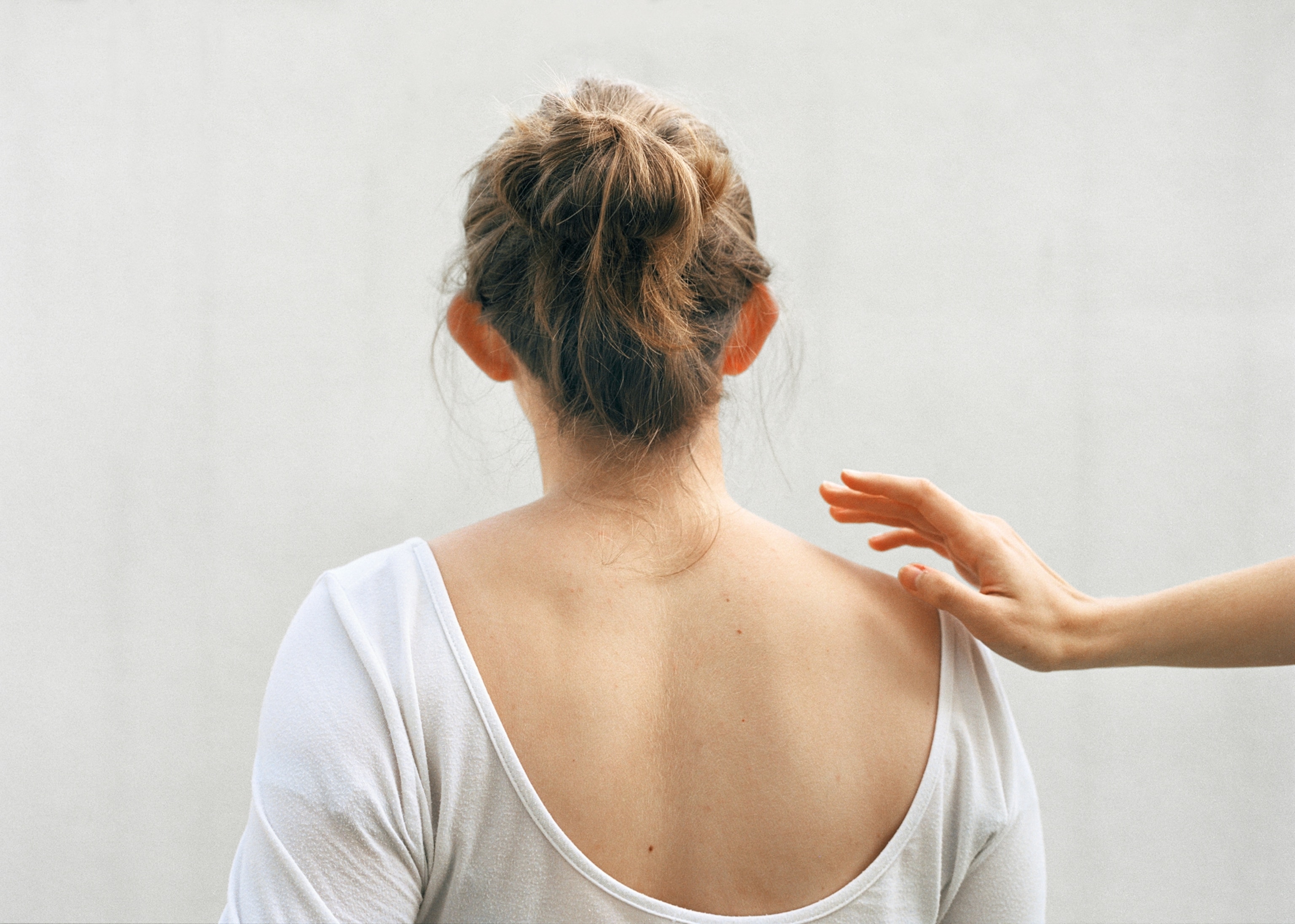 A young woman is seen from behind as a hand reaches out gently to touch her back