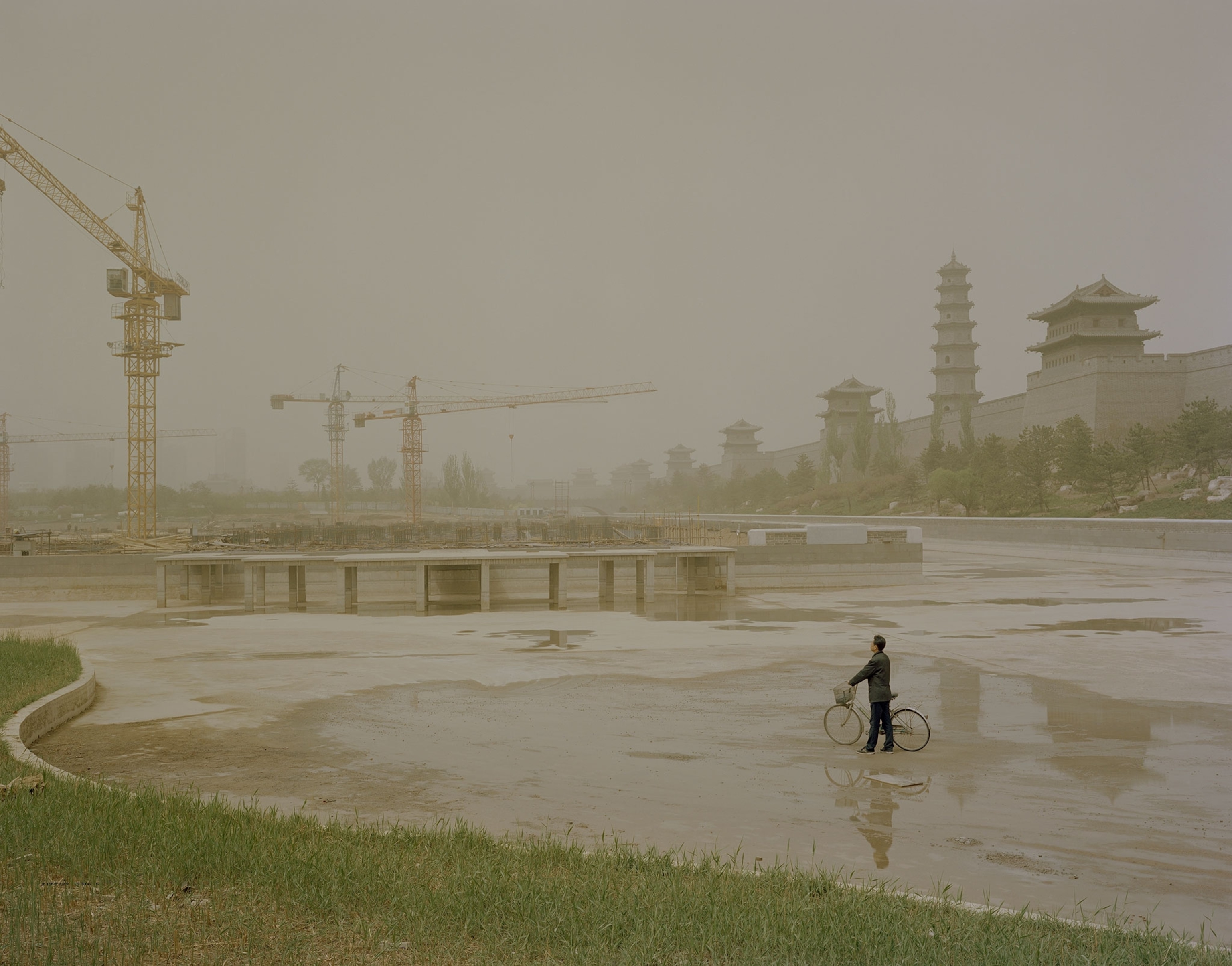 a man with a bicycle and cranes in the background