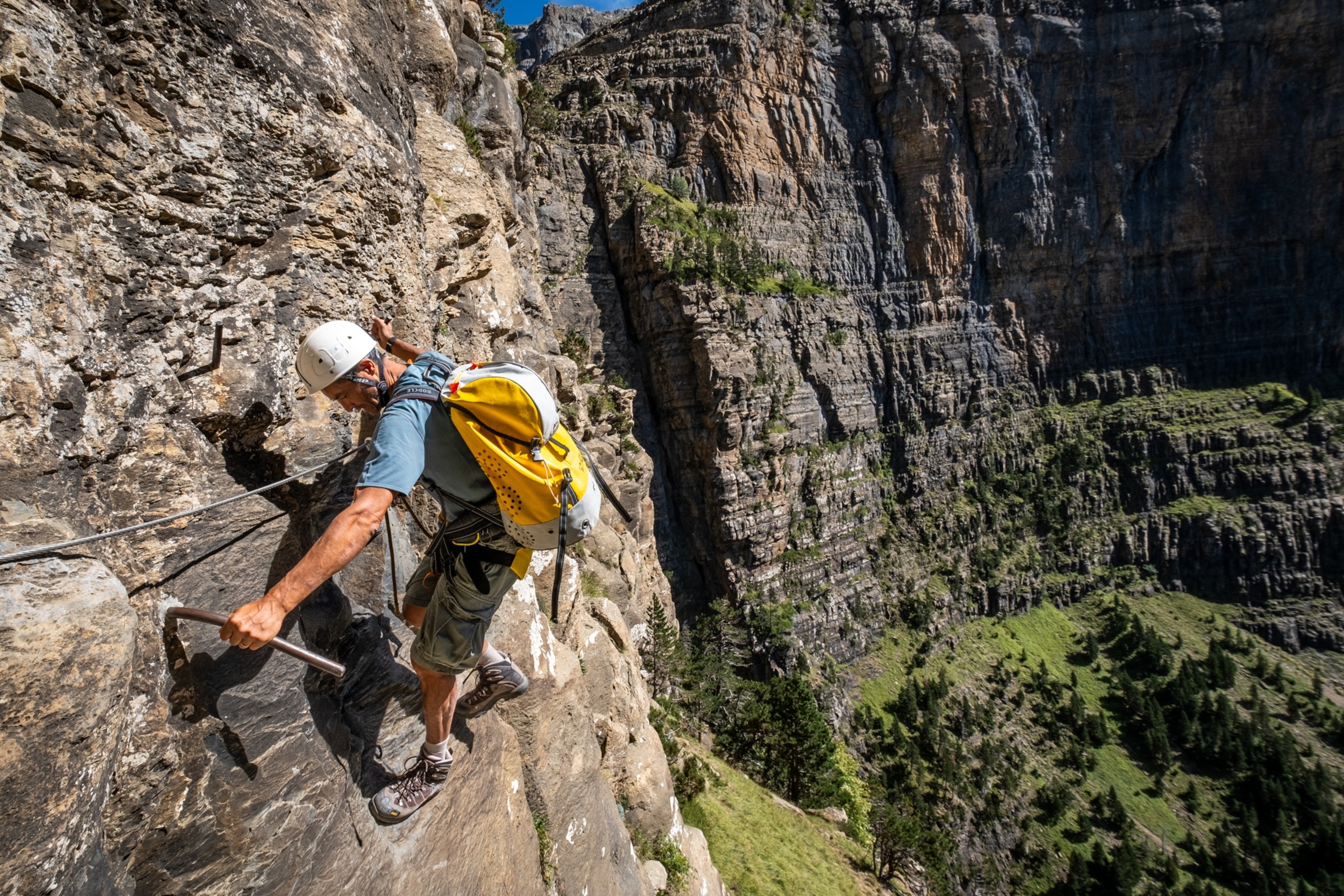 A man climbing on the side of a cliff, with a white helmet.