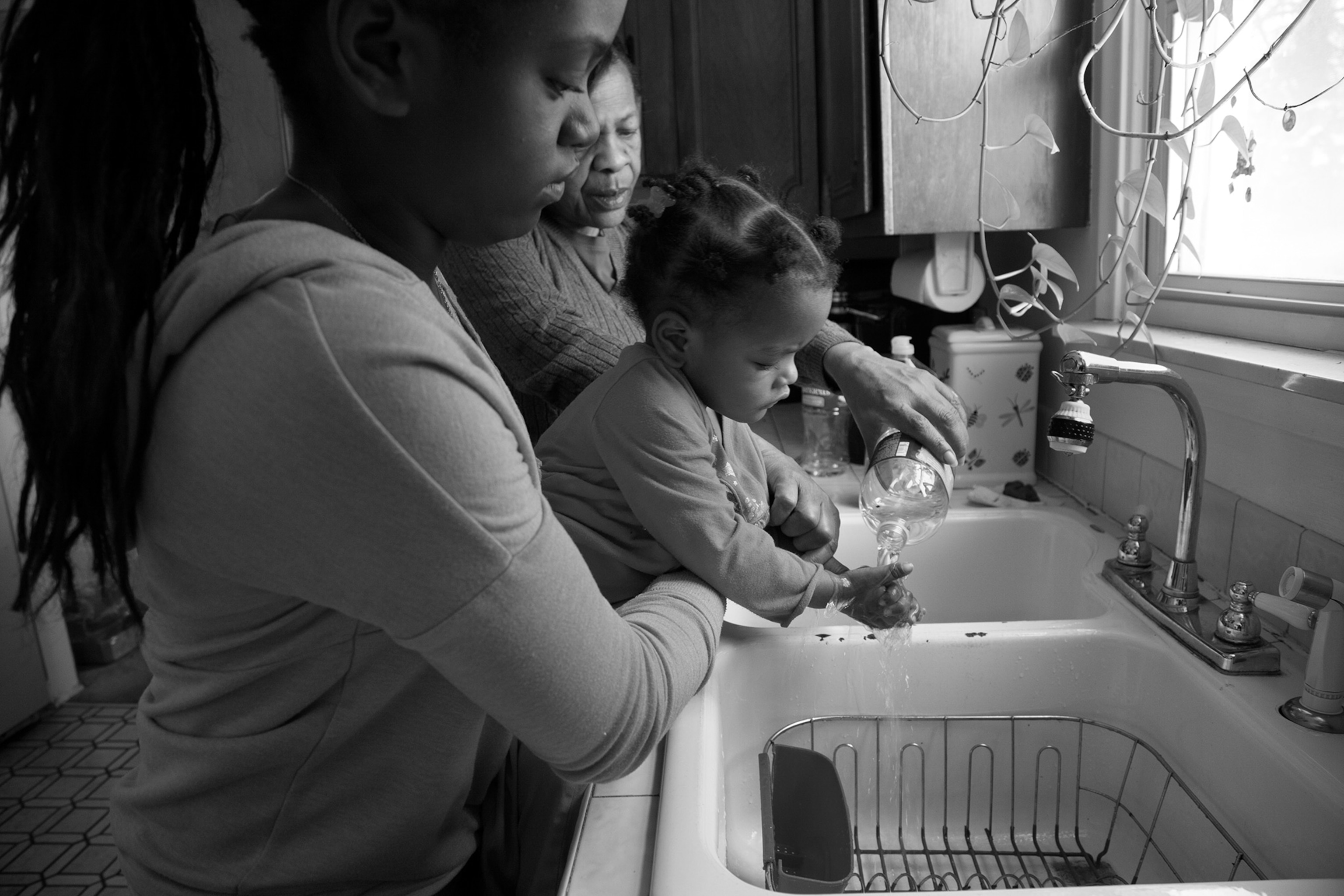 women helping young girl wash hands with bottled water