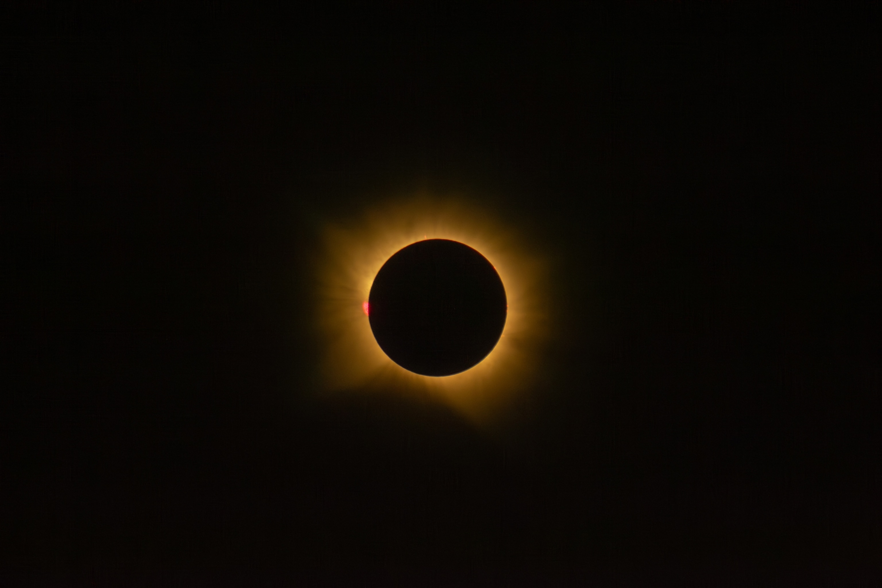 A black solar disk eclipses the Sun, surrounded by a glowing golden corona against a dark sky