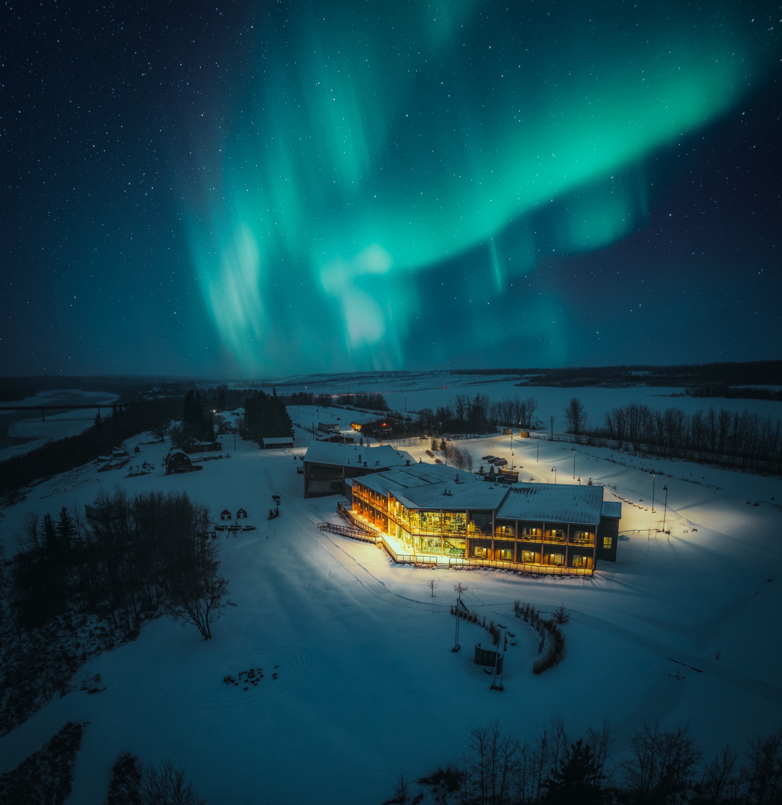 A snowy landscape featuring a hotel under a starry sky with vibrant northern lights.