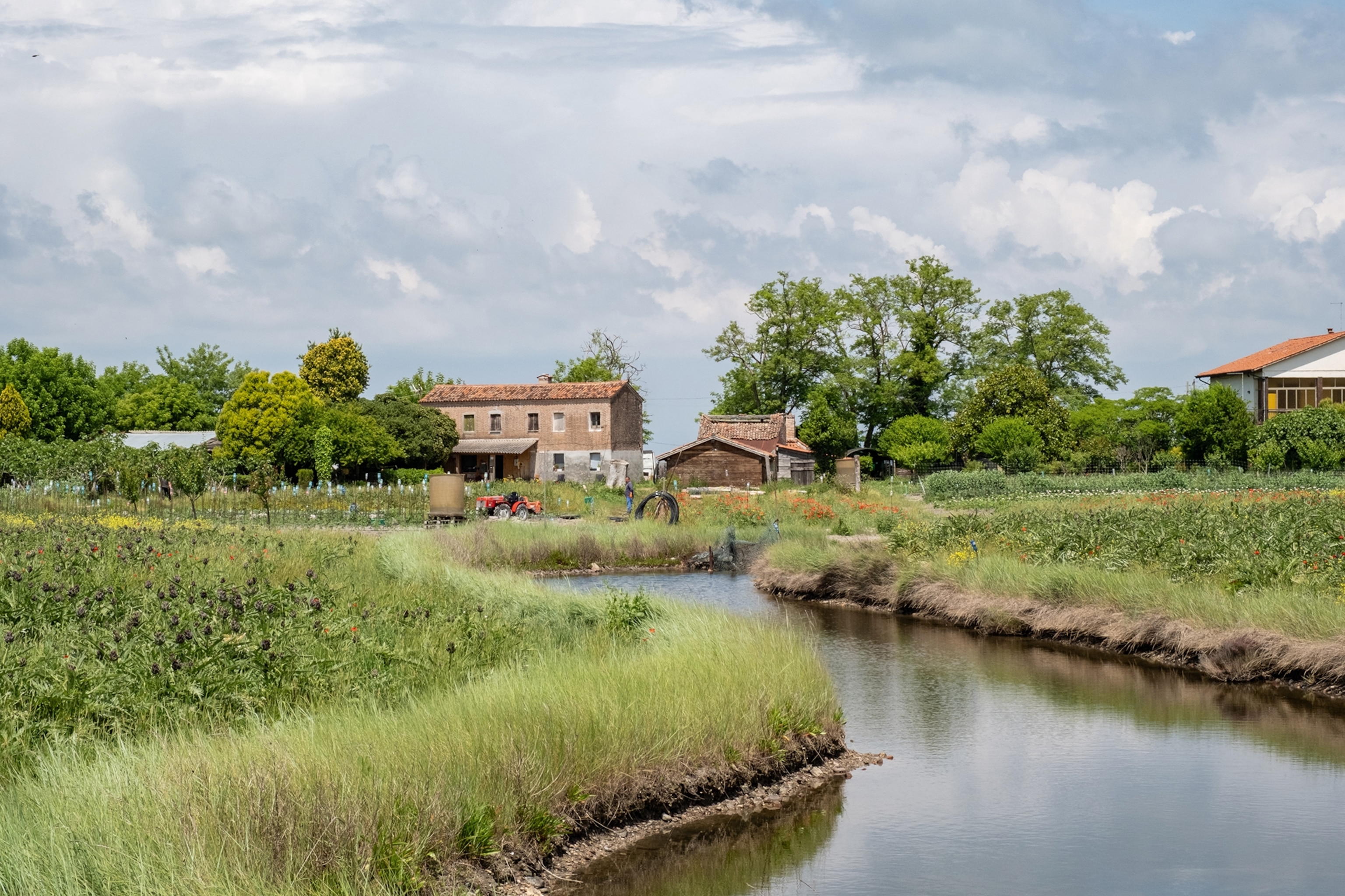 A view onto Italian, sloping marshlands running towards a farm and stone house.