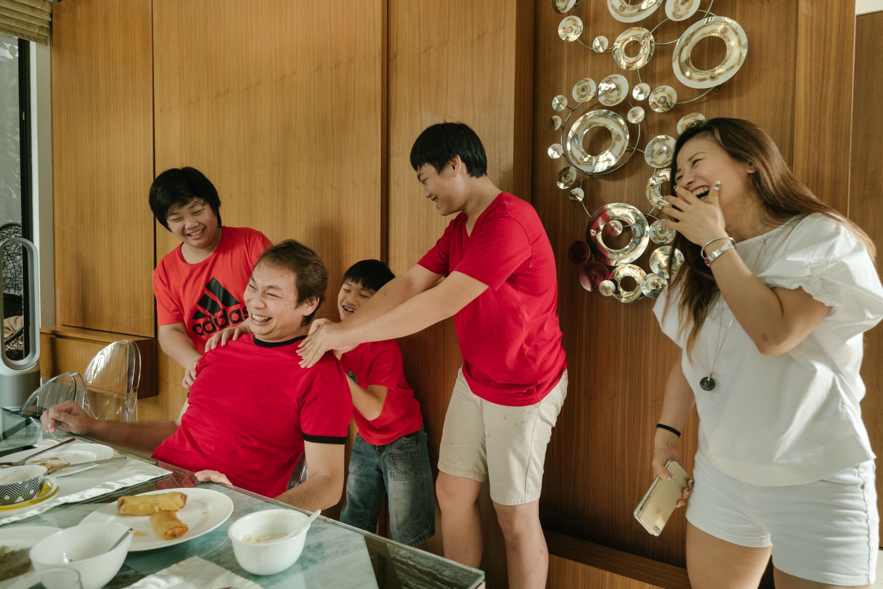 laughing man getting a massage from his sons as his wife looks on, Singapore.