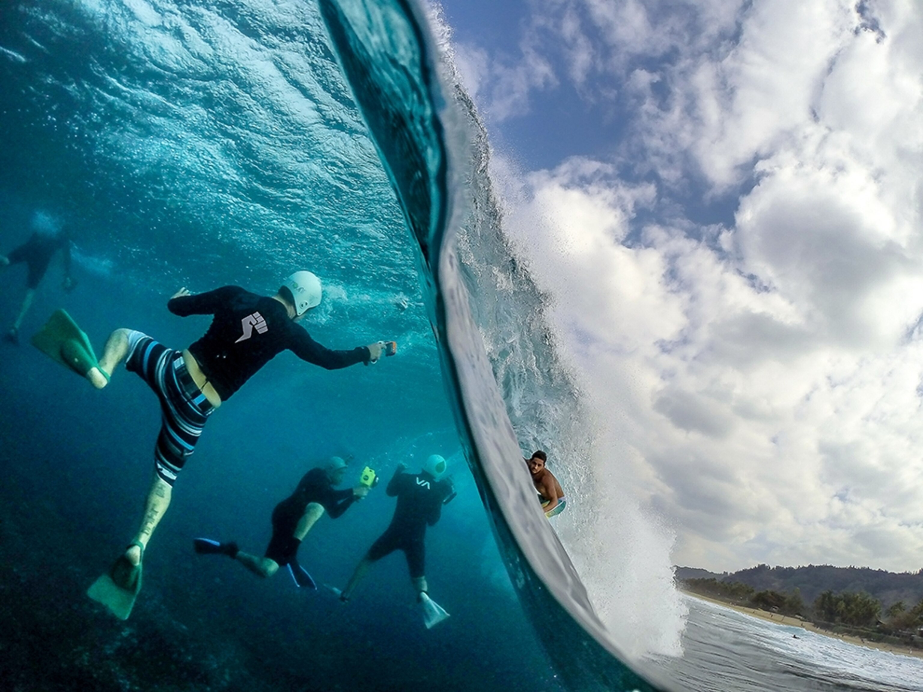 a surfer riding a wave and being photographed by a group of underwater photographers.