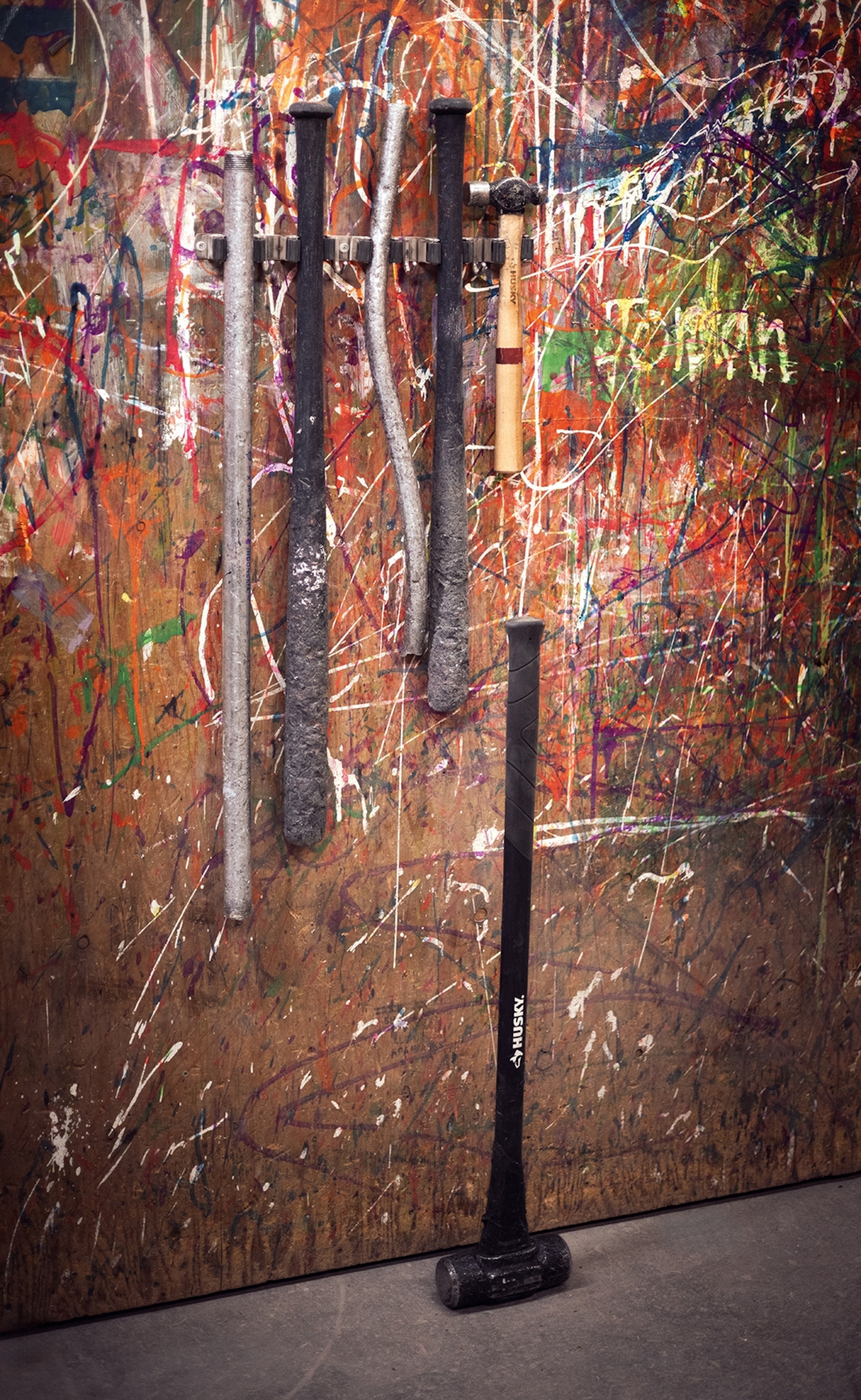 A close-up of bats and hammers hung on a plywood wall with trickles of paint.