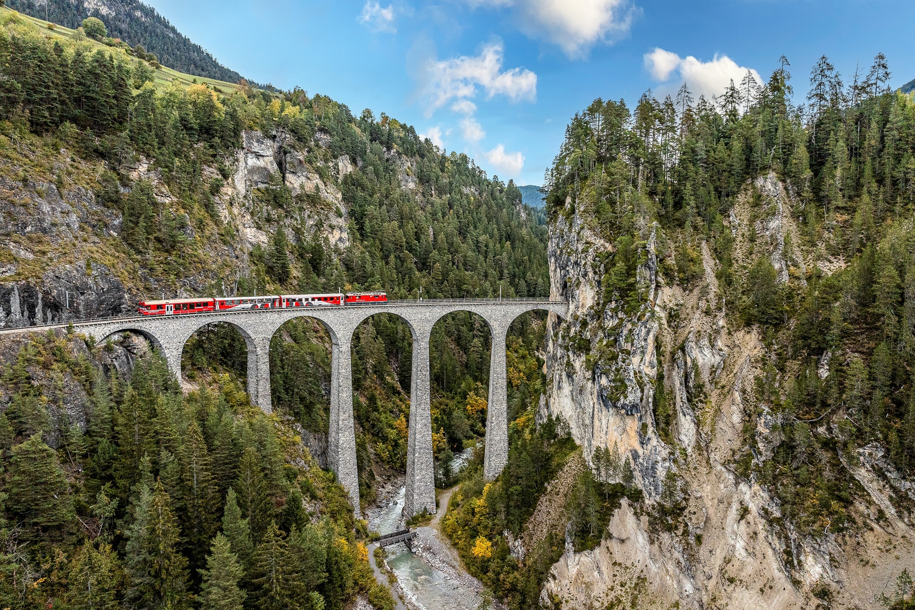 A train passes over the Landwasser Viaduct amid lofty mountains and trees