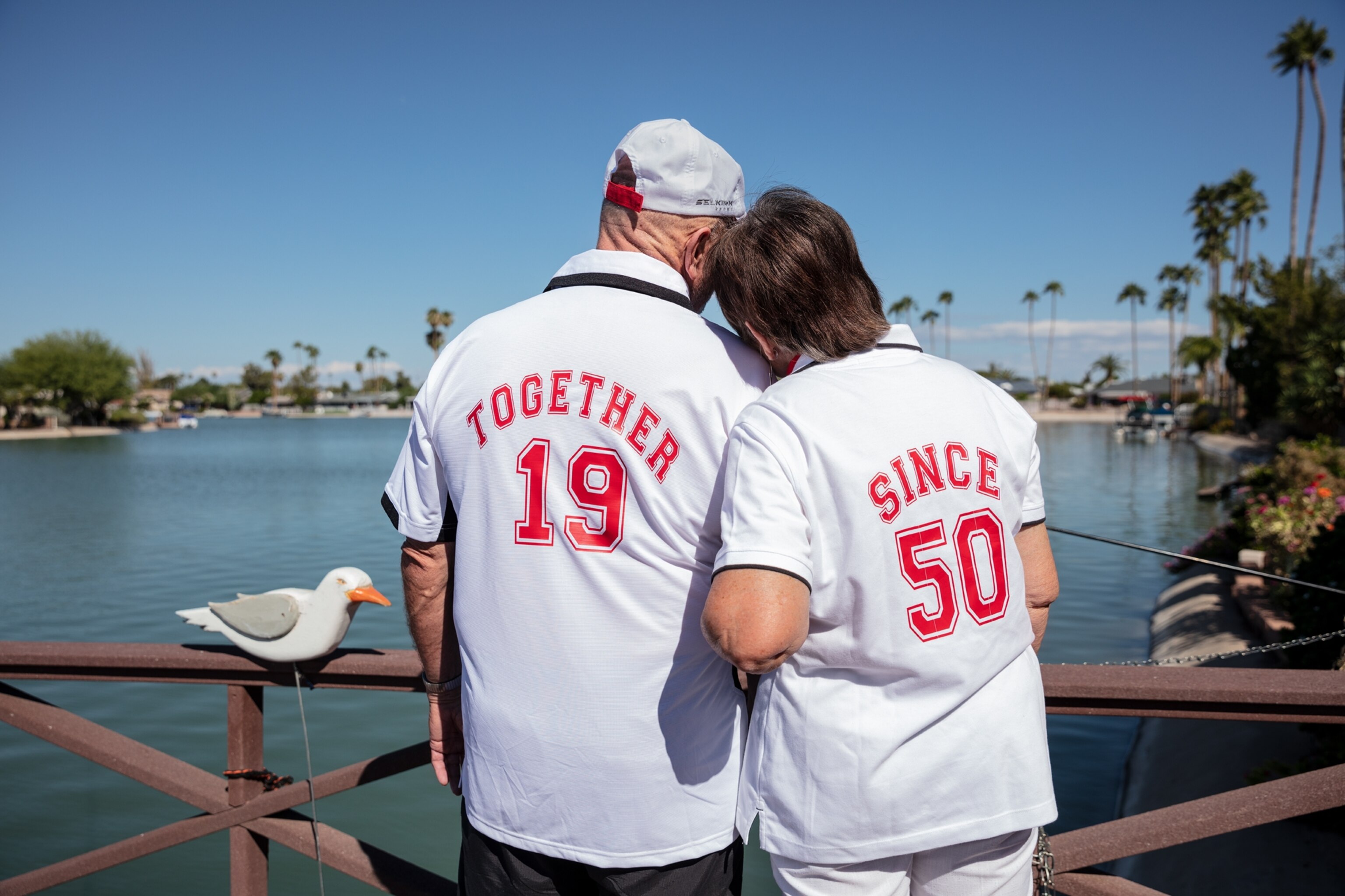 Picture of view from behind at a couple in white t-shirts with printed "Together since 1950" on the backs.