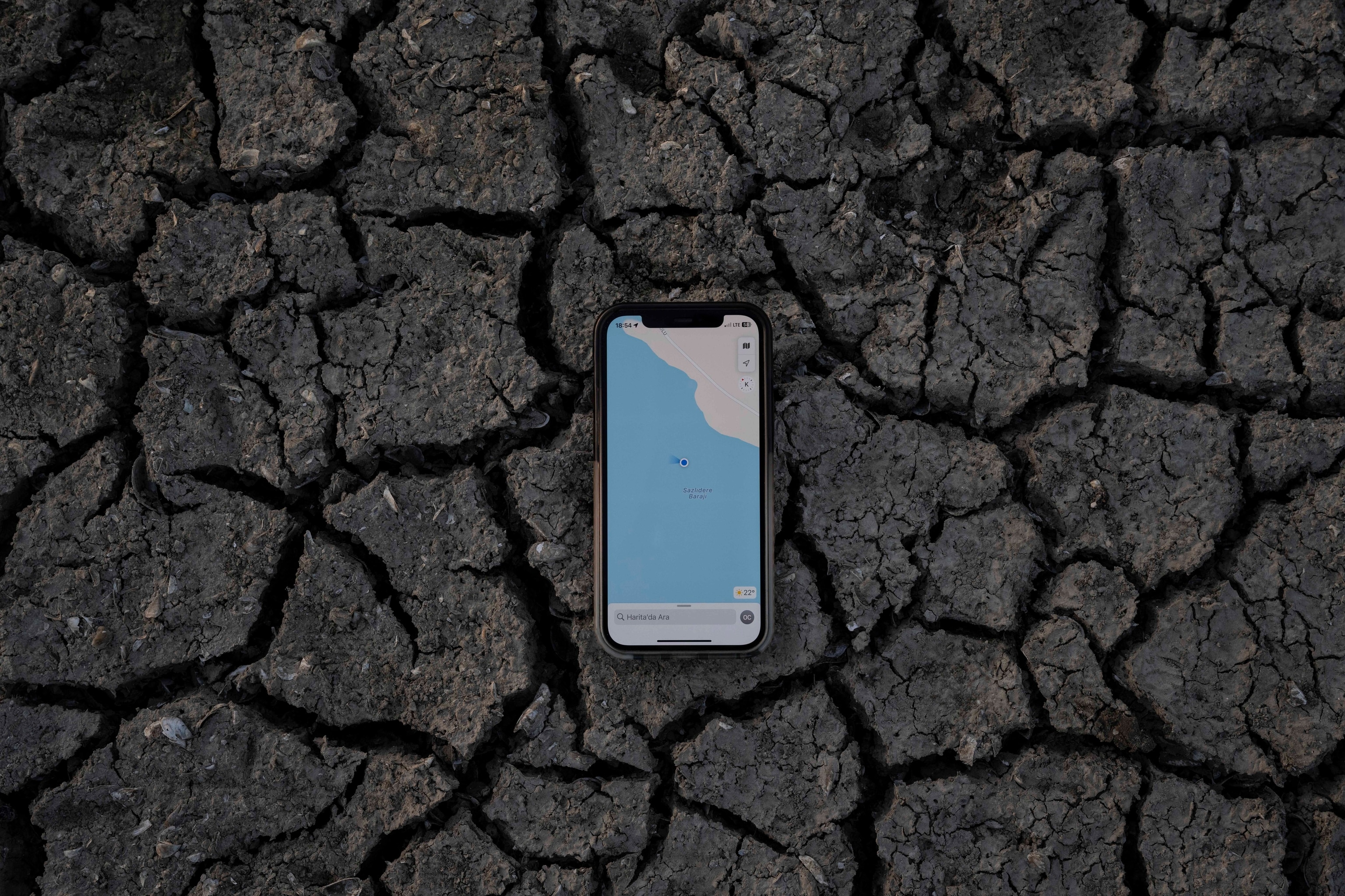 Cracked earth under a phone shows the water on a map that once was in the area.