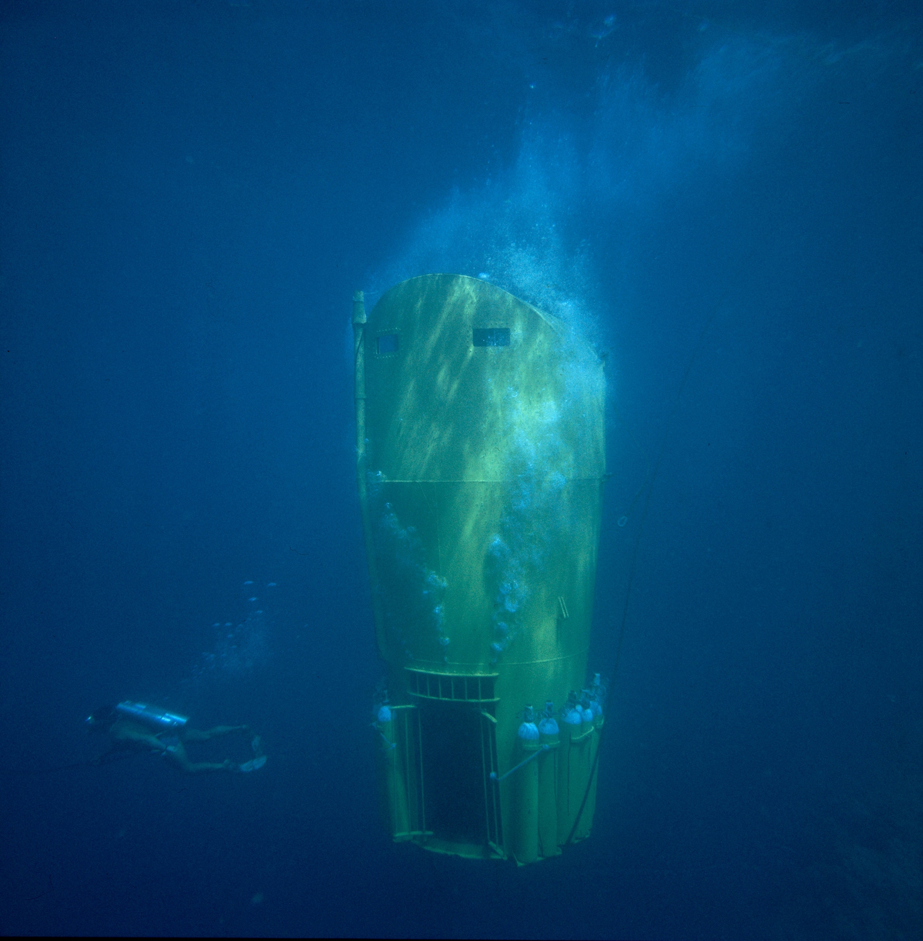A diver swims by as an underwater cabin slowly descends.