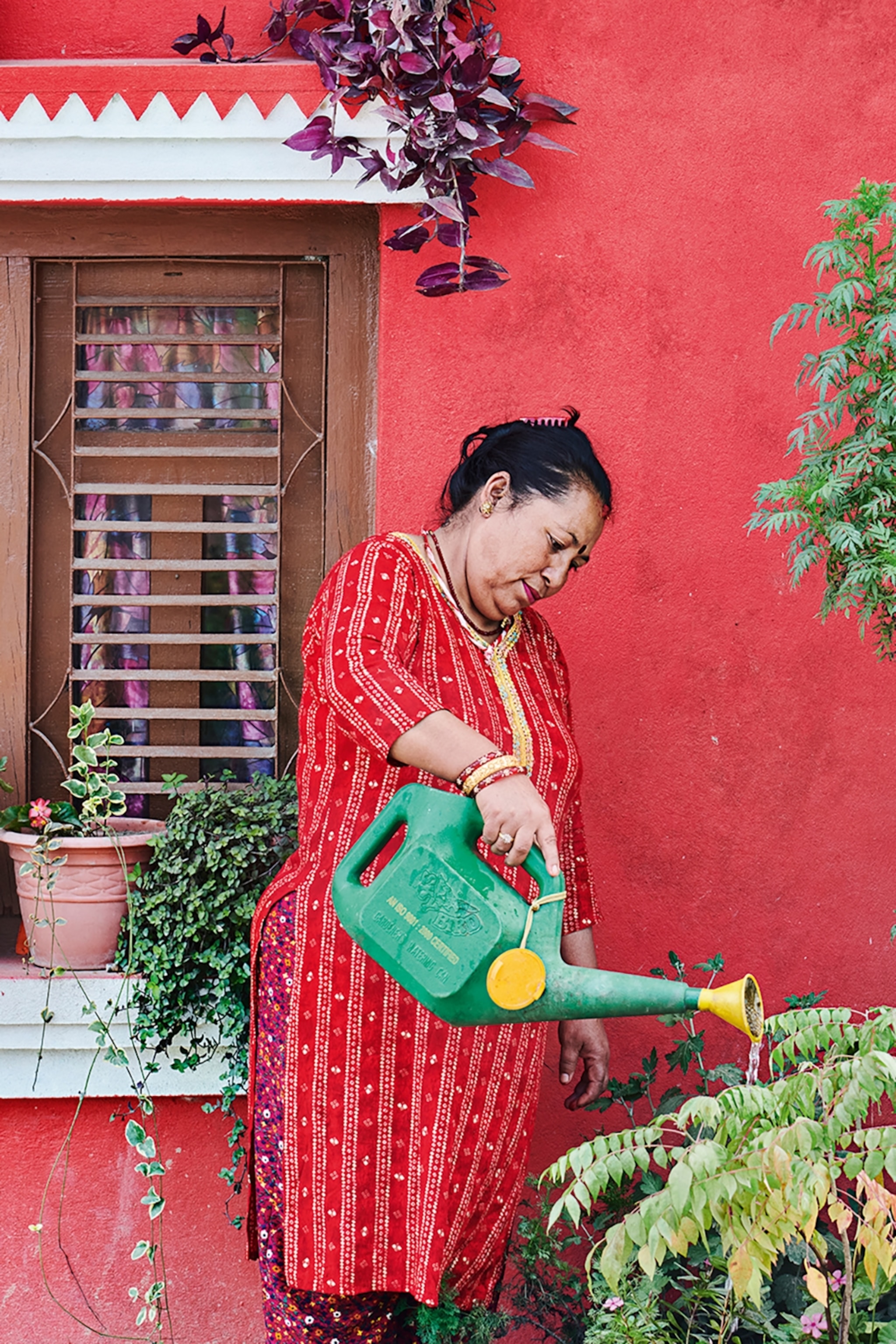 A woman in a traditional yet casual tunic tending to her lush garden in front of her house.