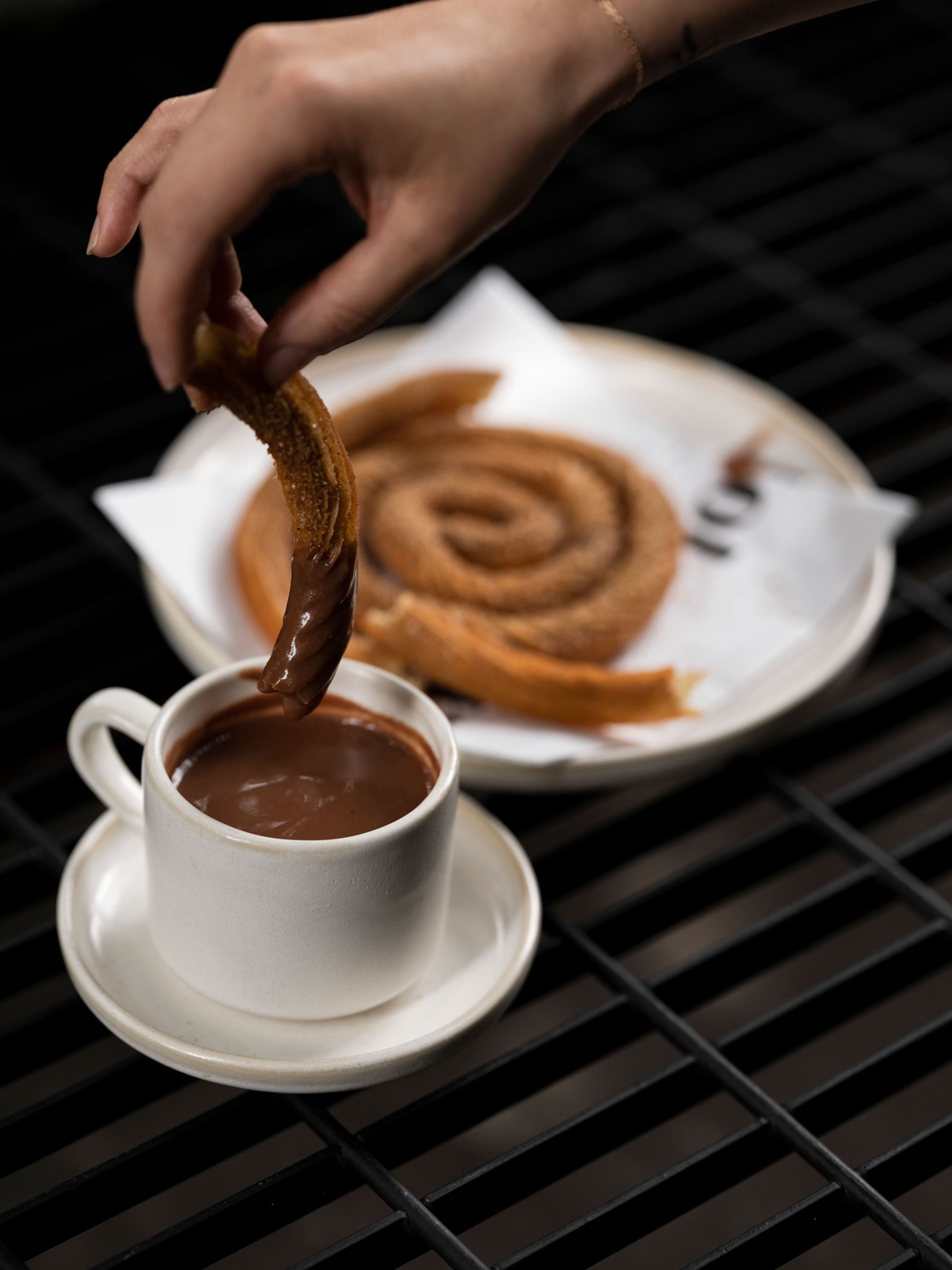 A hand dipping a churro into a chocolate like sauce