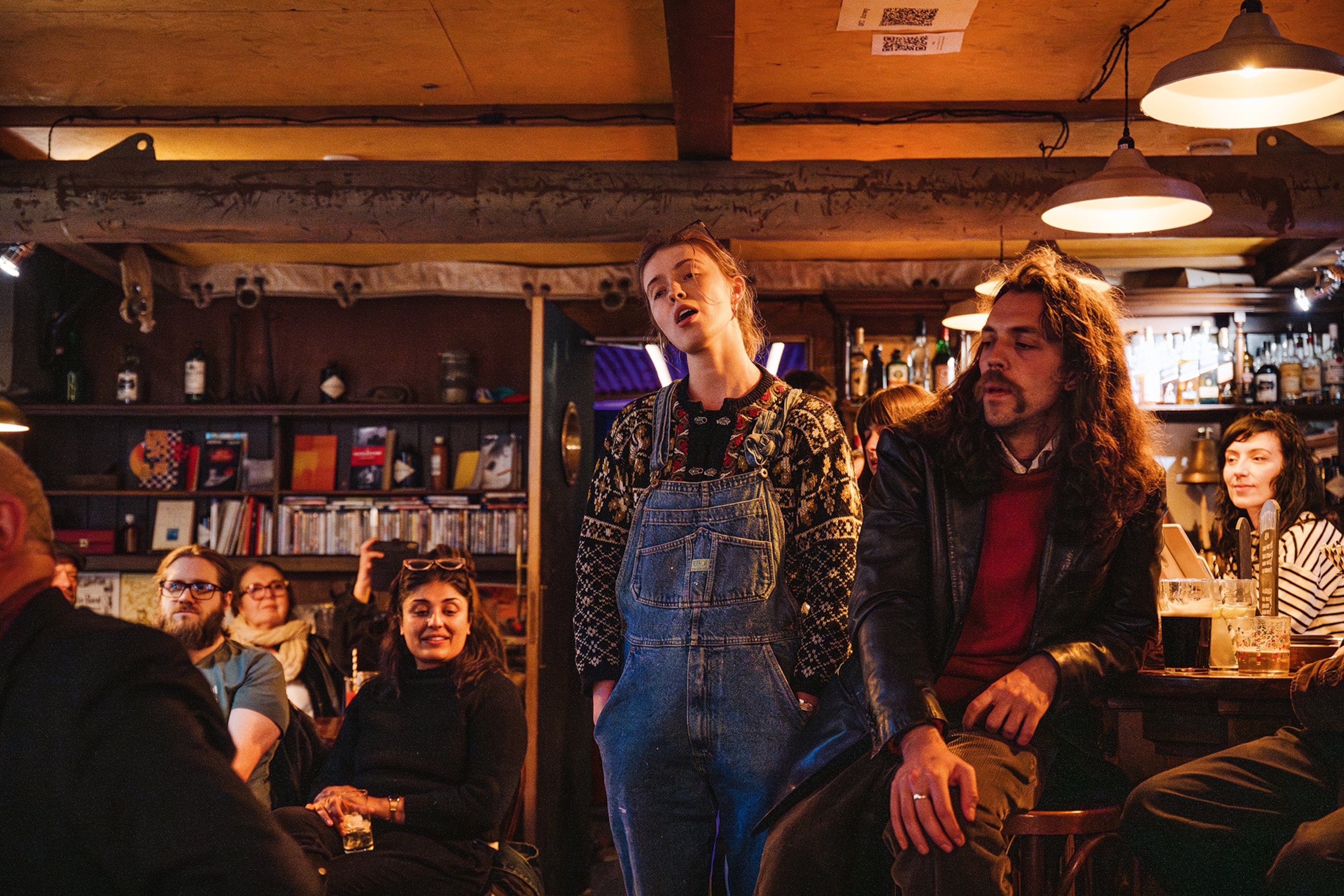 A woman singing in a pub surrounded by other guests.