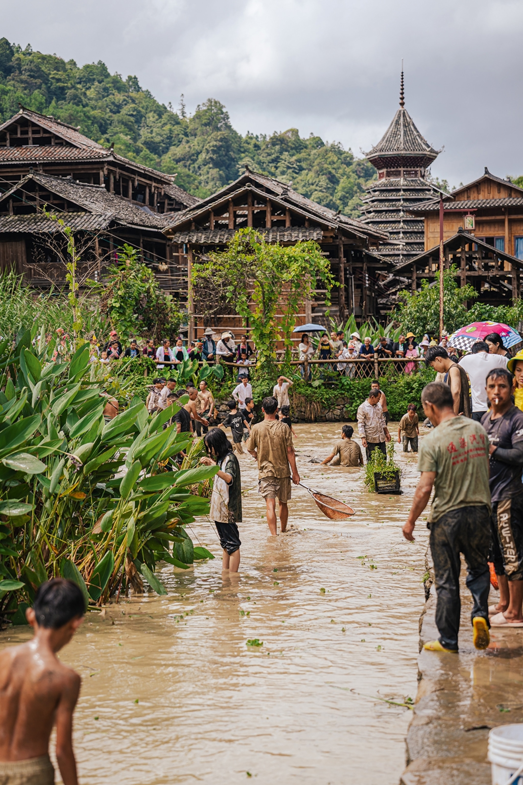 A narrow river snaking through wooden houses with lots of local villagers bathing and catching fish.