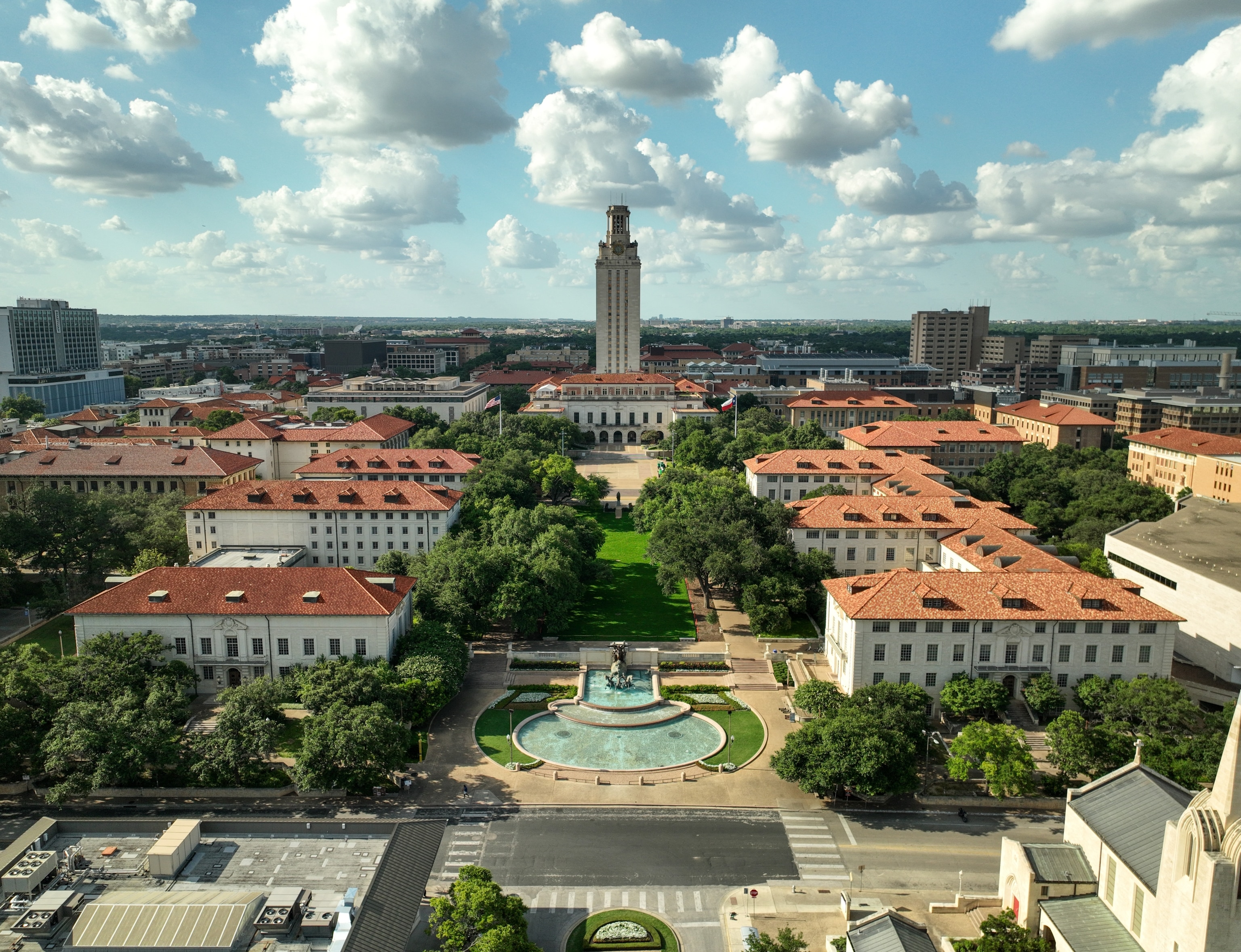 Aerial view of college campus with fountain in the middle and white buildings with red roofs.