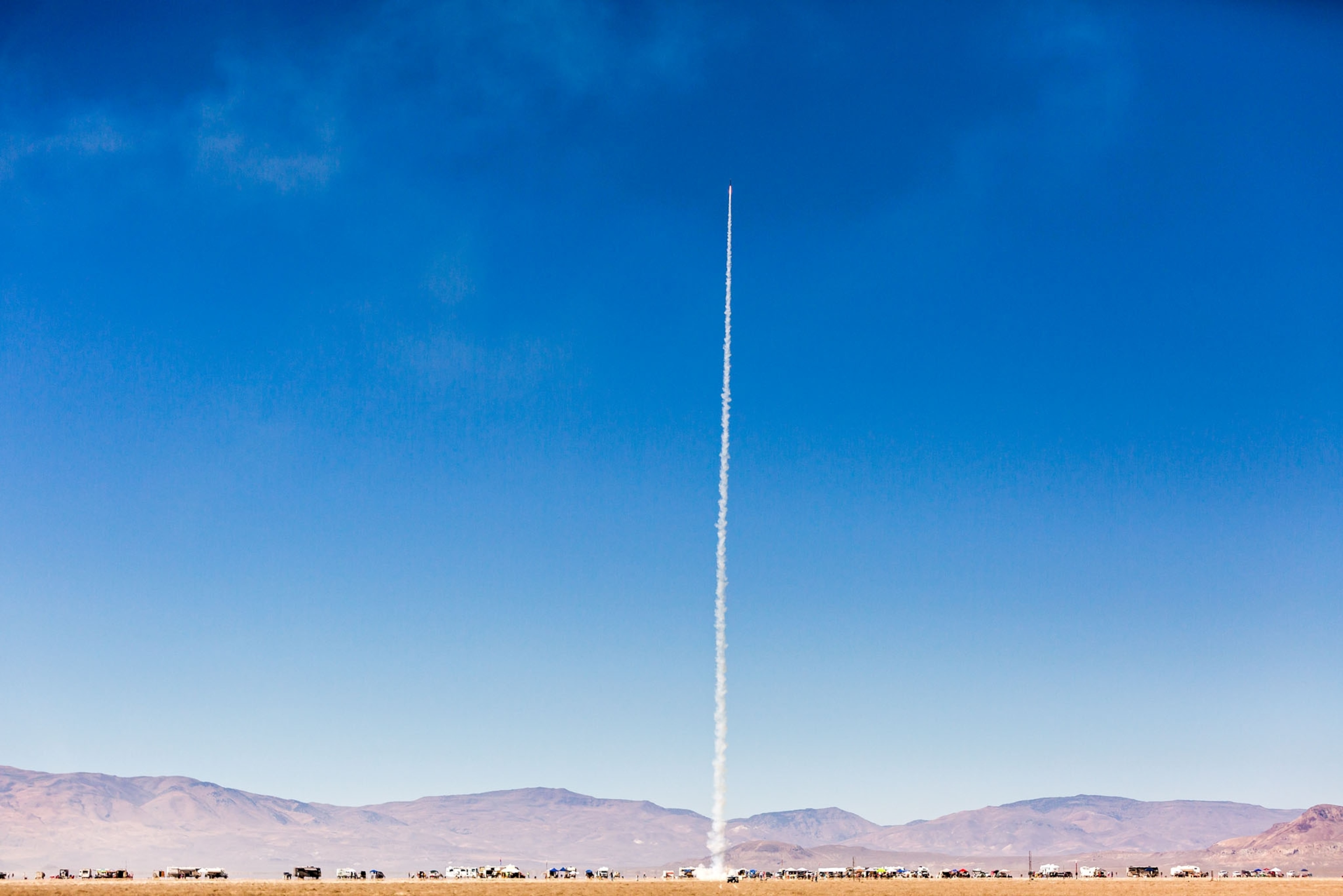 a rocket launched into the air leaving a white trail on a blue sky day in the desert