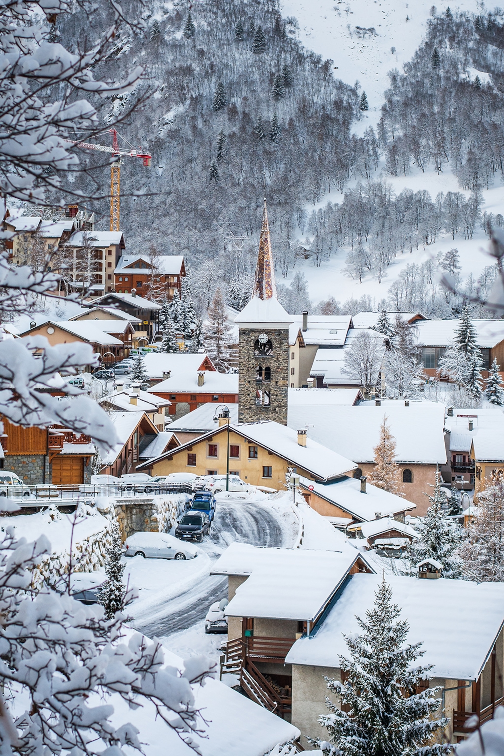 A snowy mountain village shot through pine trees on a hill.