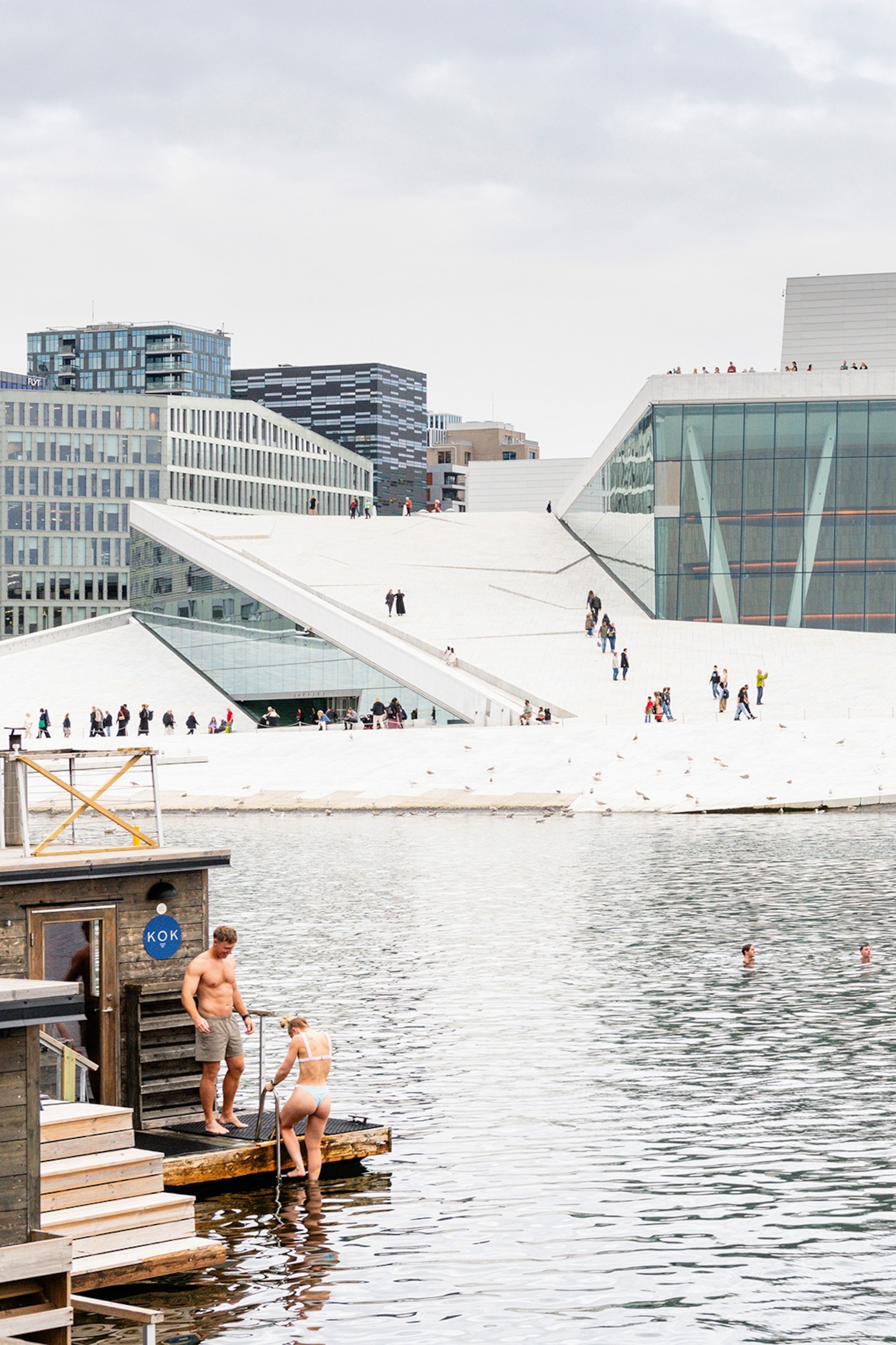 People going swimming at a harbour promenade on a cloudy day.