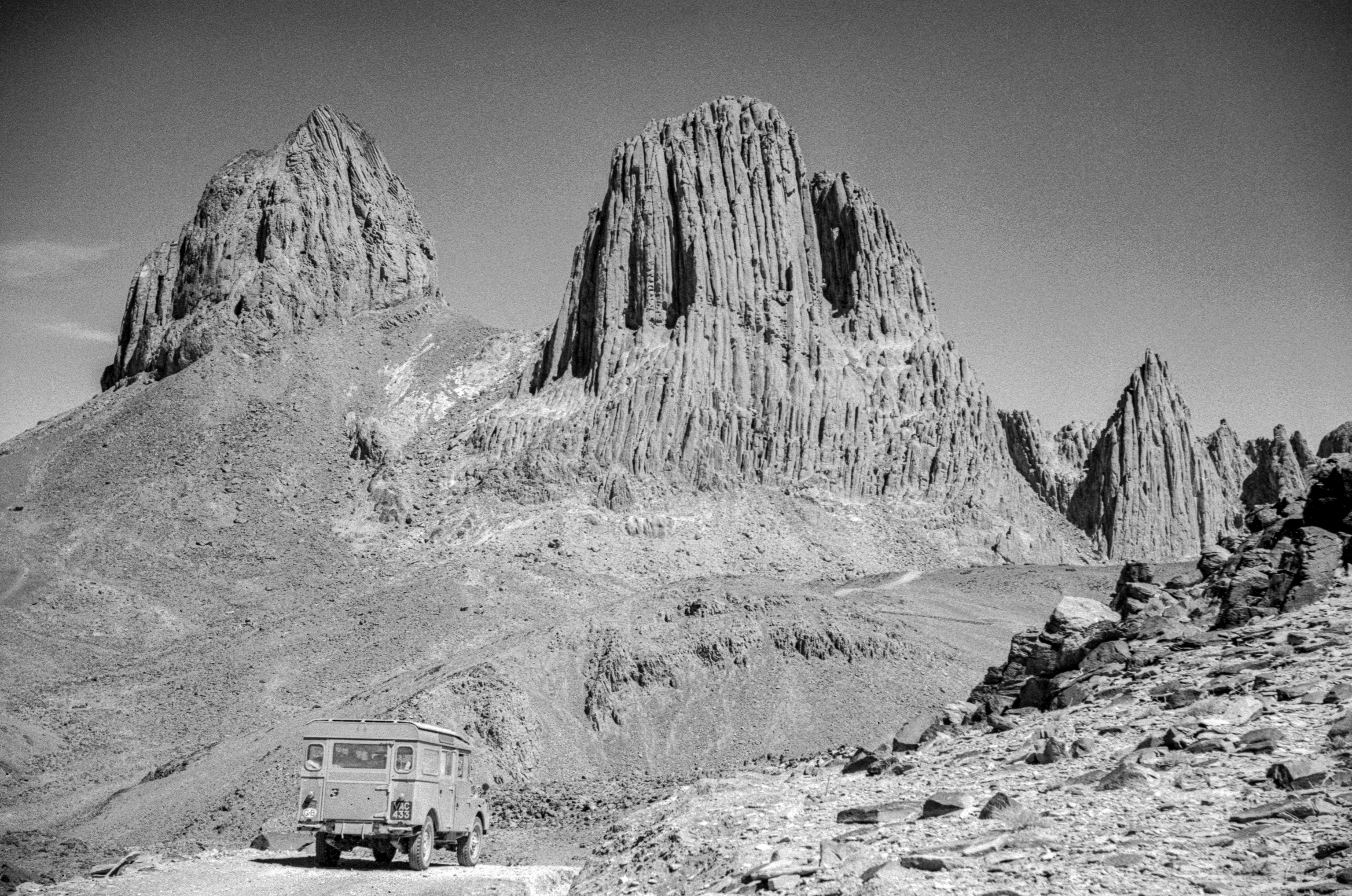 A car is on a road in front of rocky landscape.