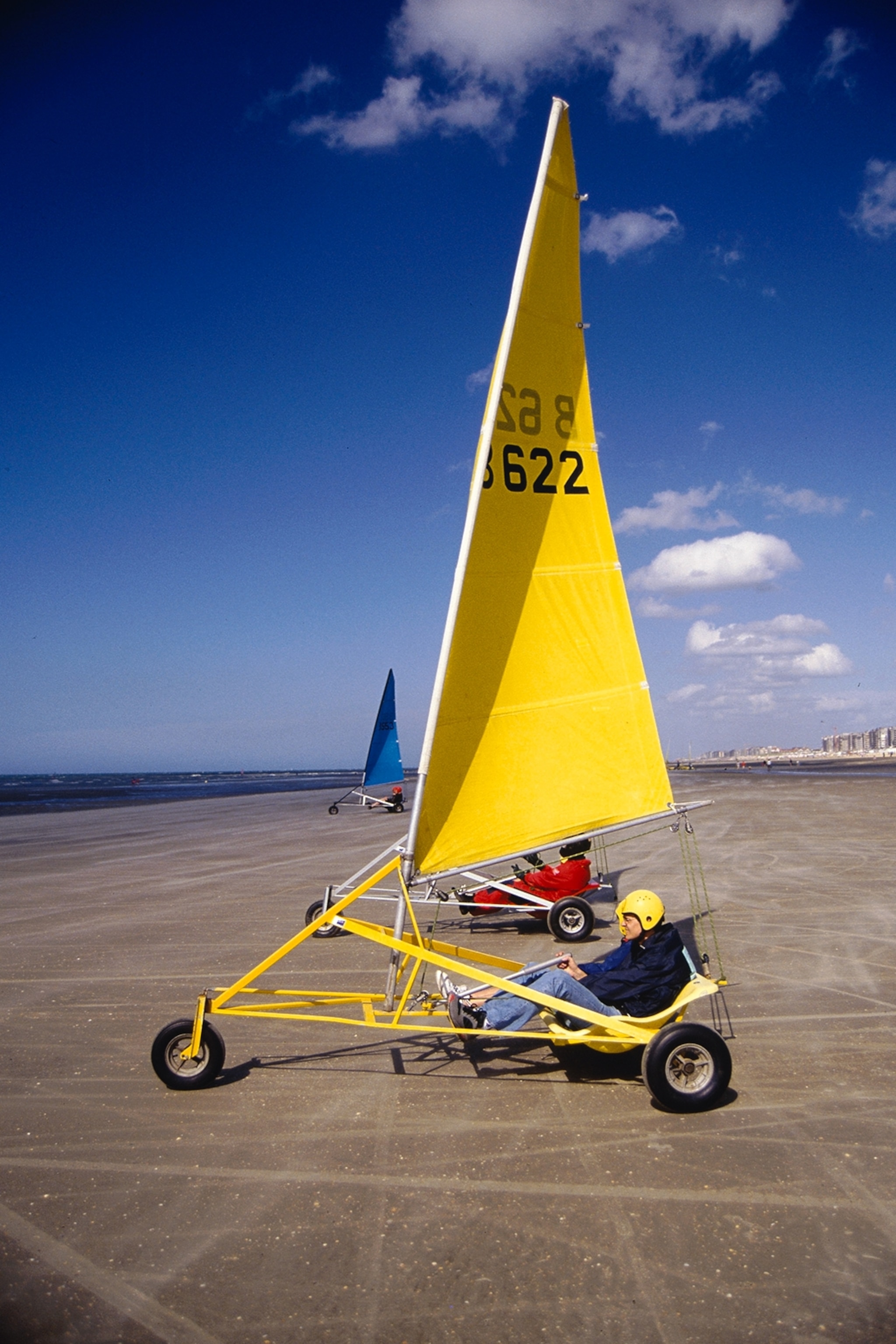 A yellow sand sail buggy on the beach with blue sky.