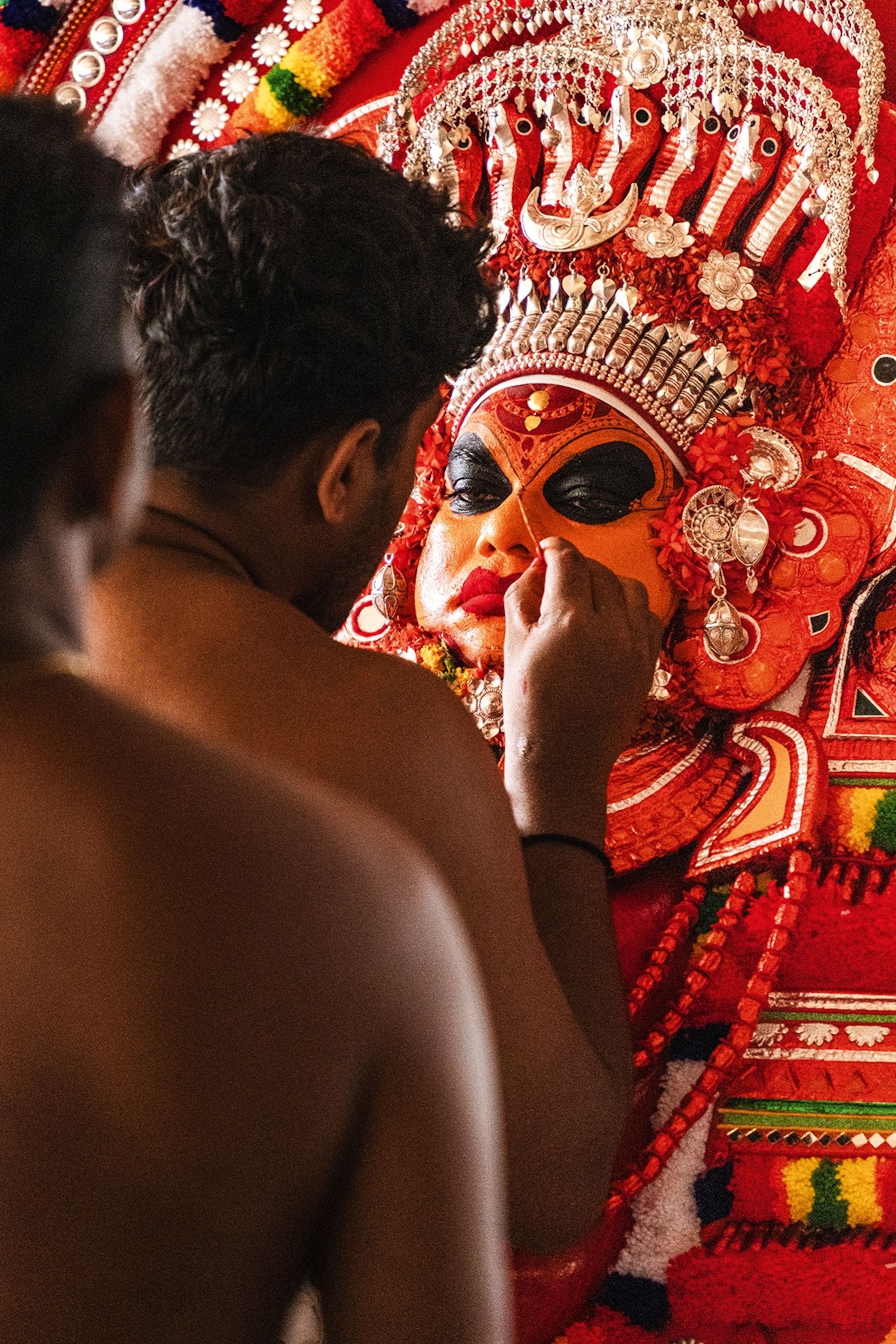 An intimate shot of a local man painting the face of a costumed man opposite him with striking patterns.