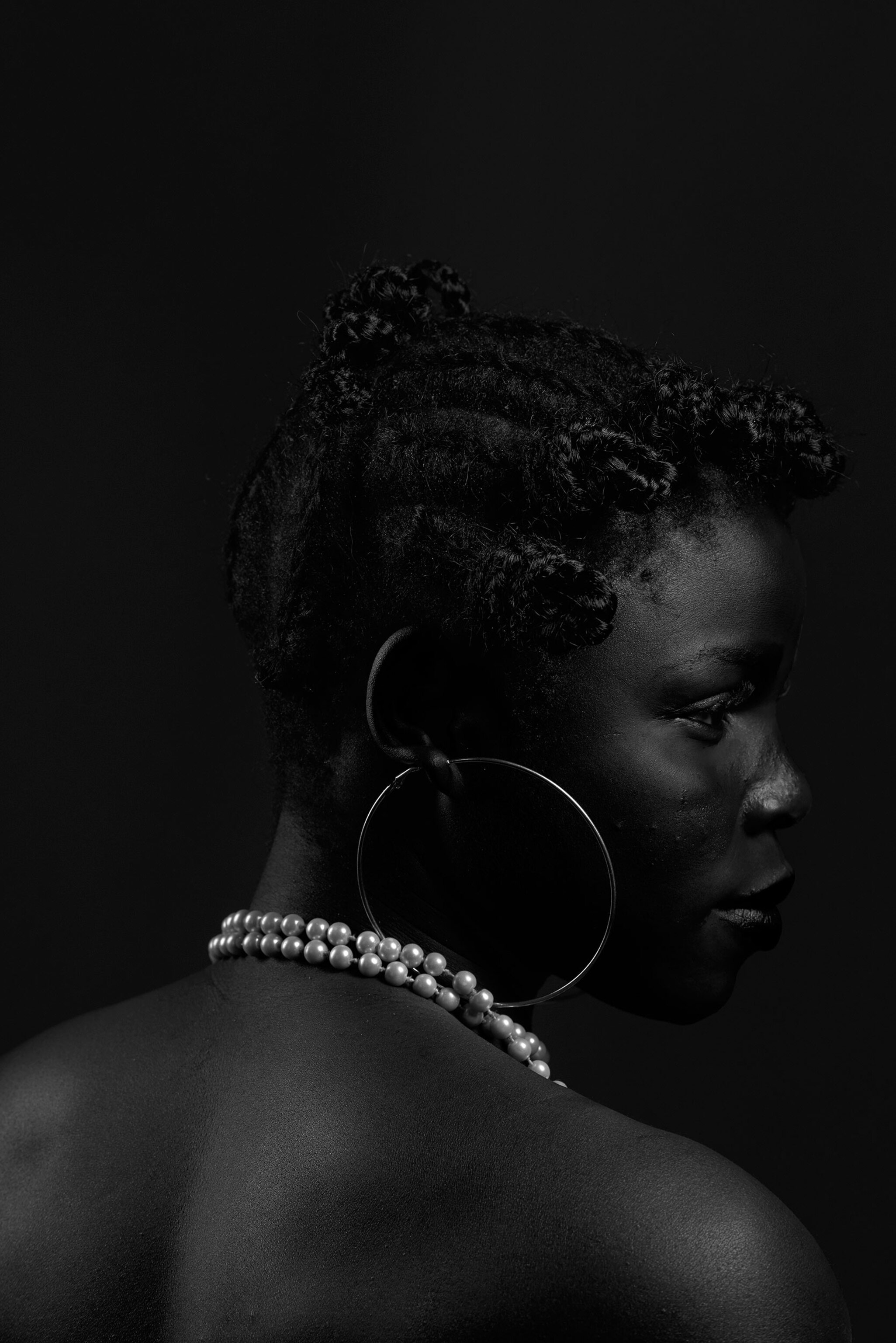 a woman in profile wearing a large hoop earring and a pearl necklace