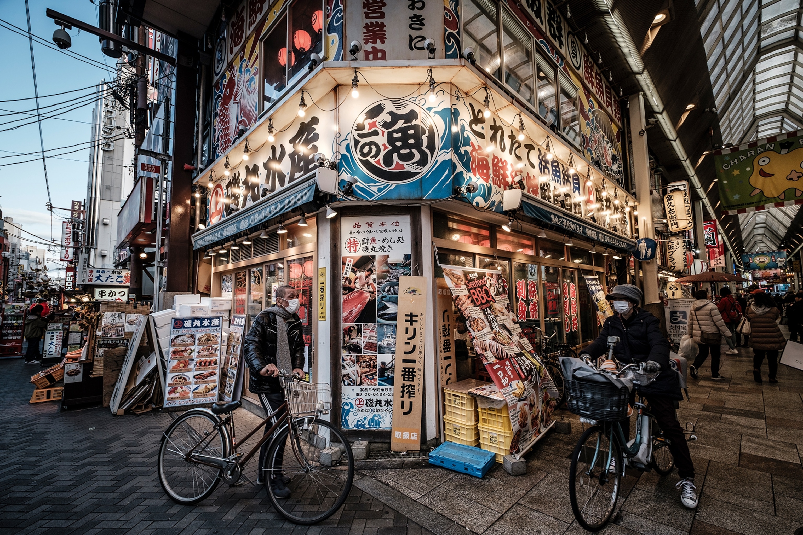 A lit-up kitchenware shop on a street corner, with signs and lamps hung around the entrance.