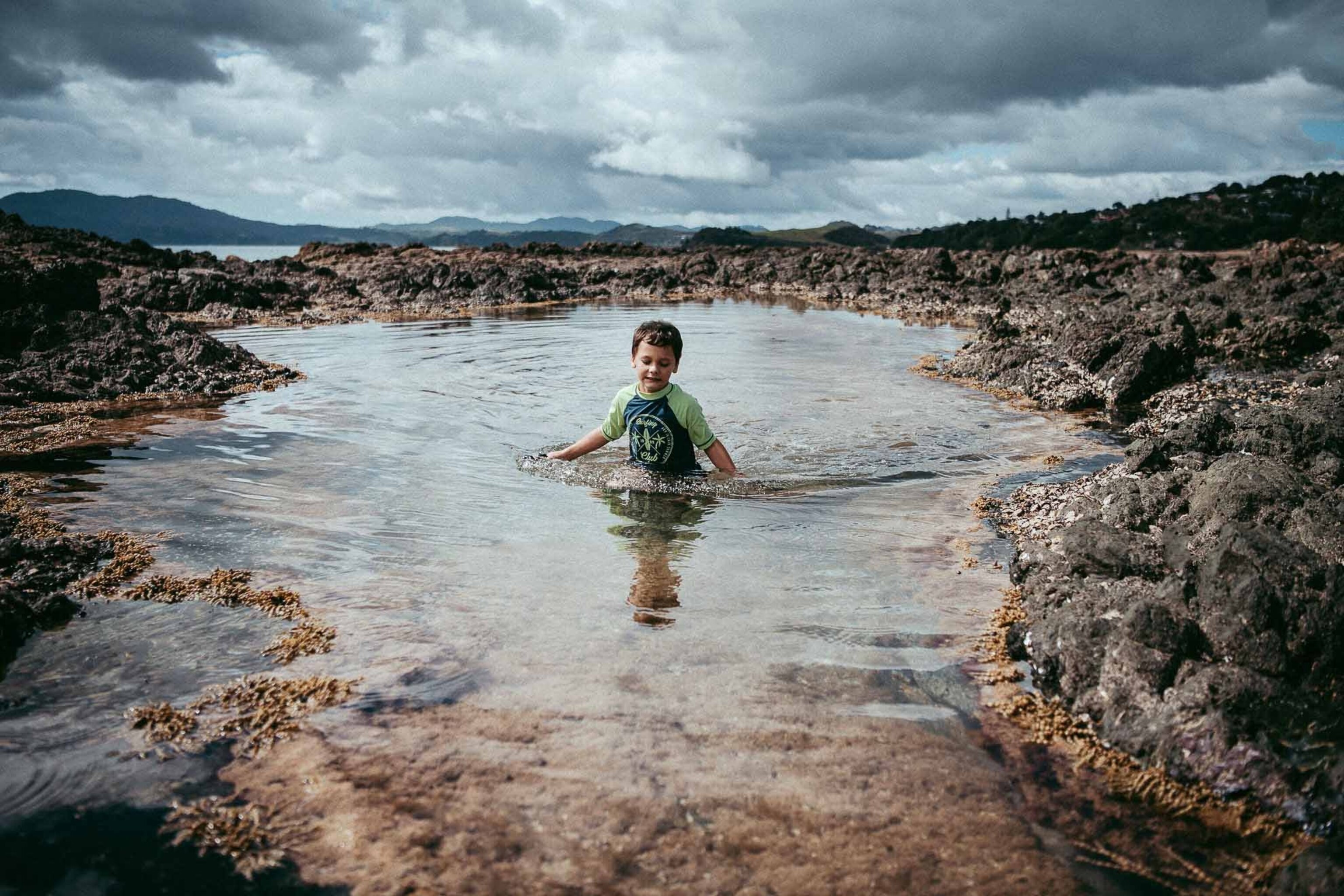 a boy walking through the water on New Zealand beach.