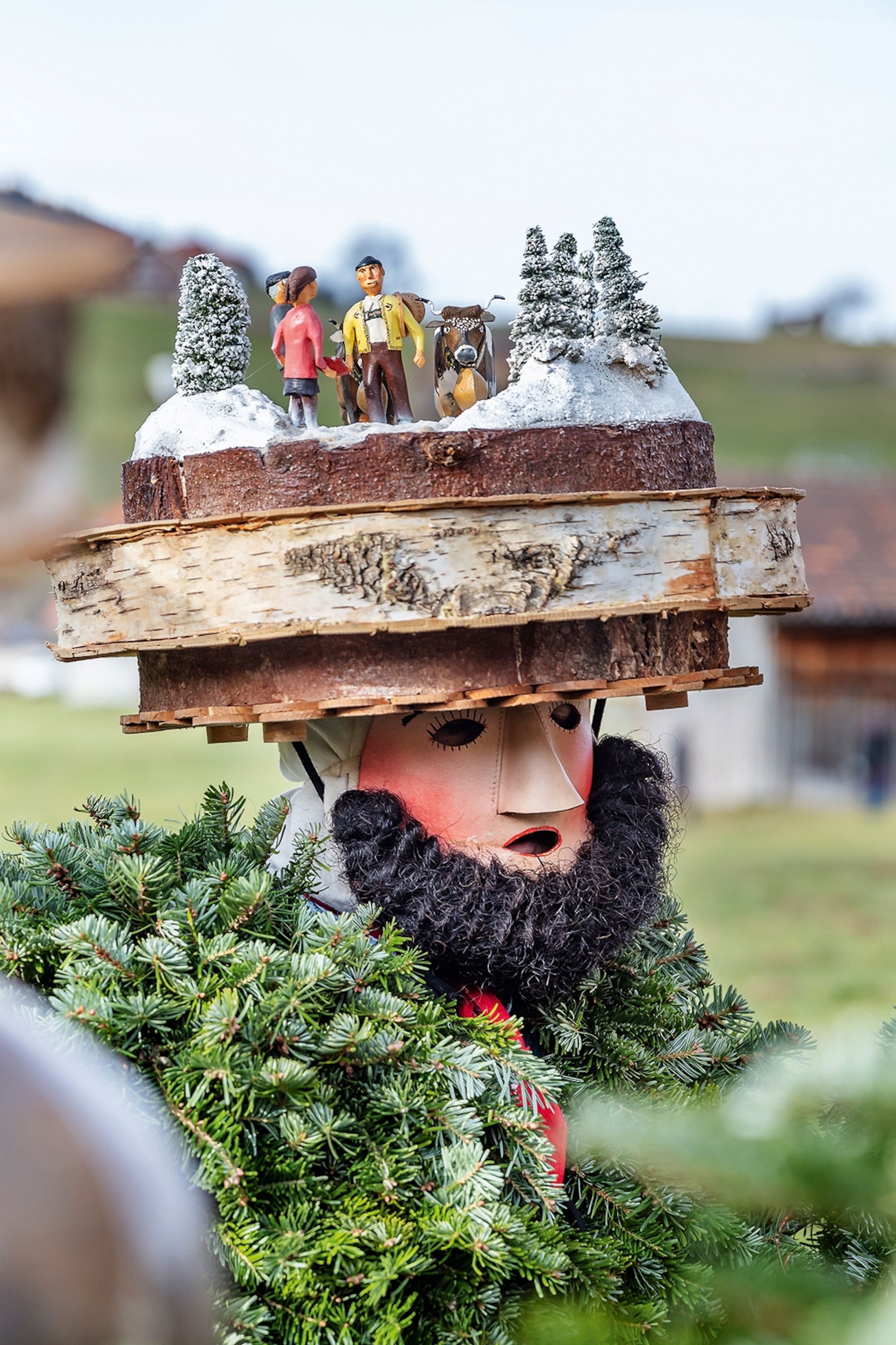 A portrait of a person wearing a wooden mask and hat with figures on its plateau.