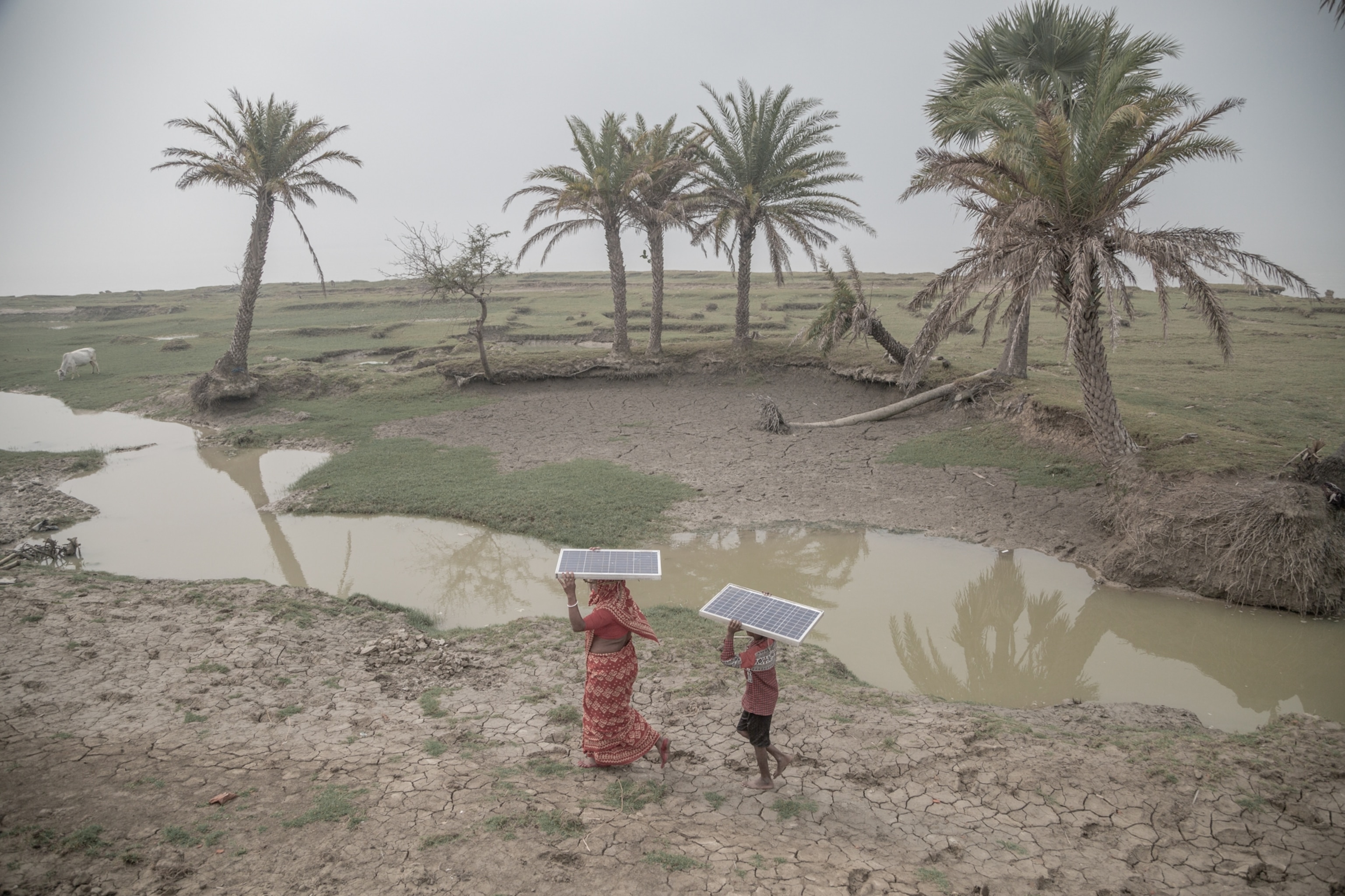 A woman and a young boy each carry a solar panel on their head in the middle of a remote island.