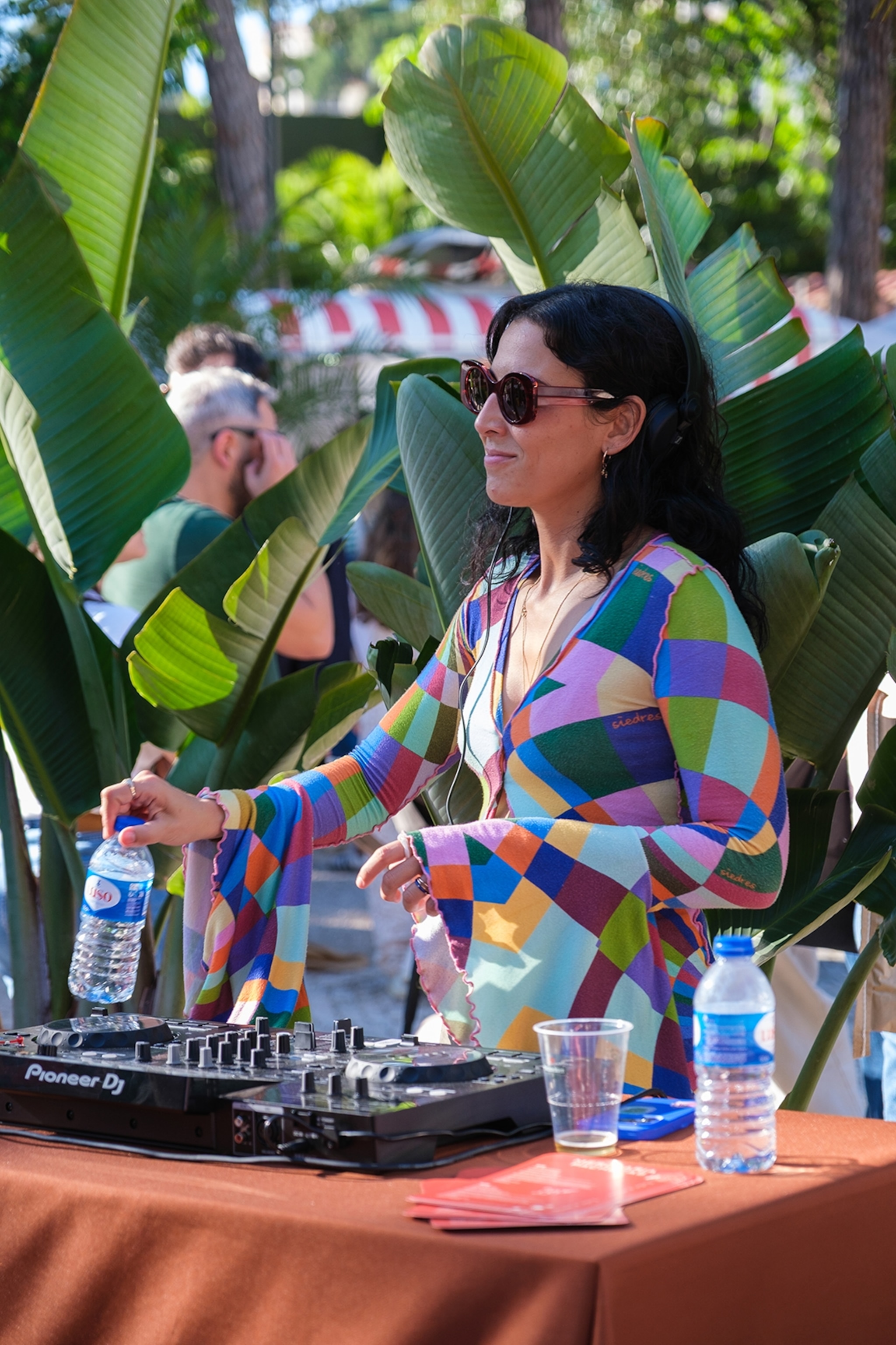 A female DJ doing an outdoor set surrounded by plants.