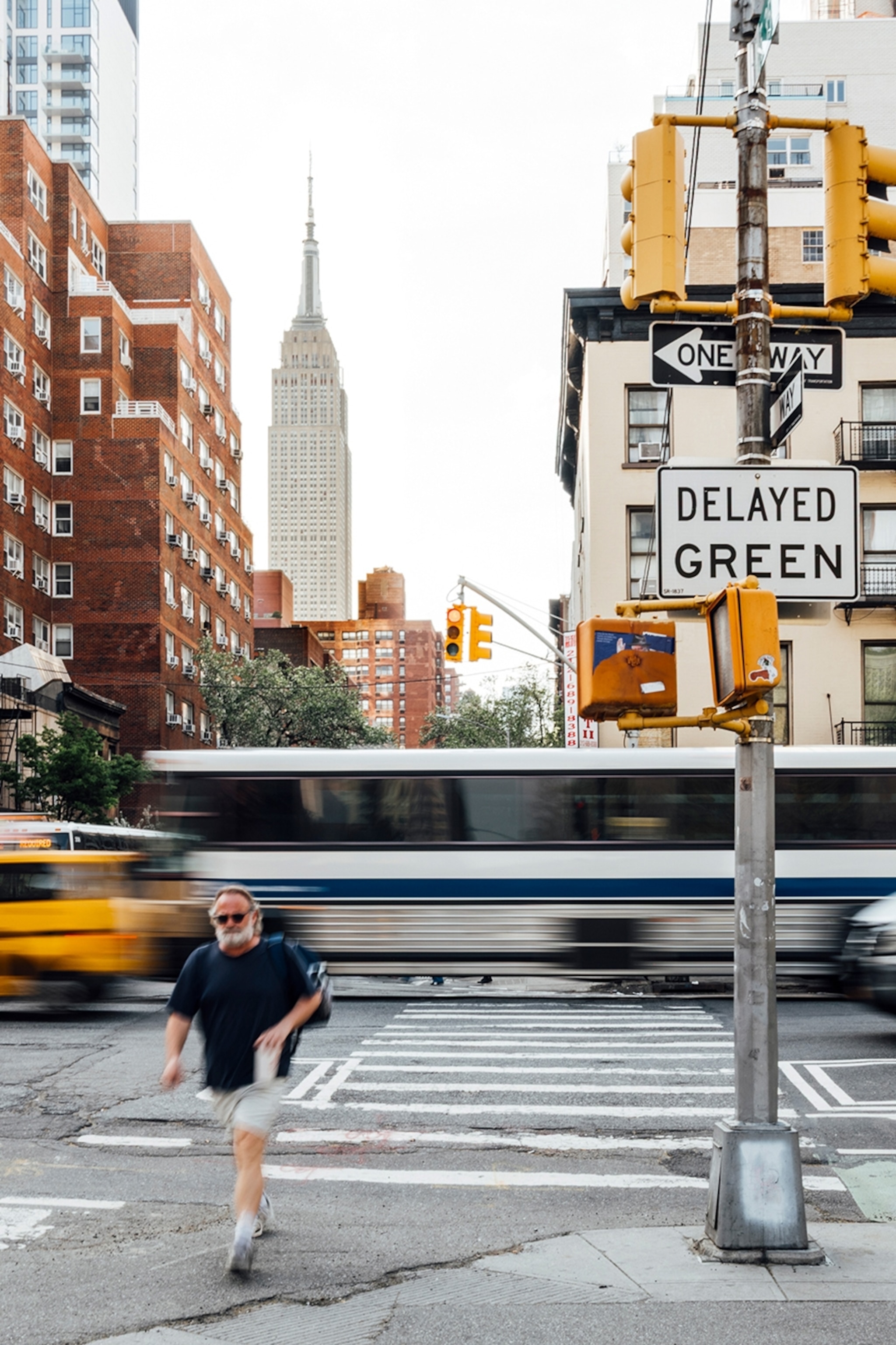 A man crossing a busy street in New York City with a yellow cab whizzing past and the Empire State Building in the distance.
