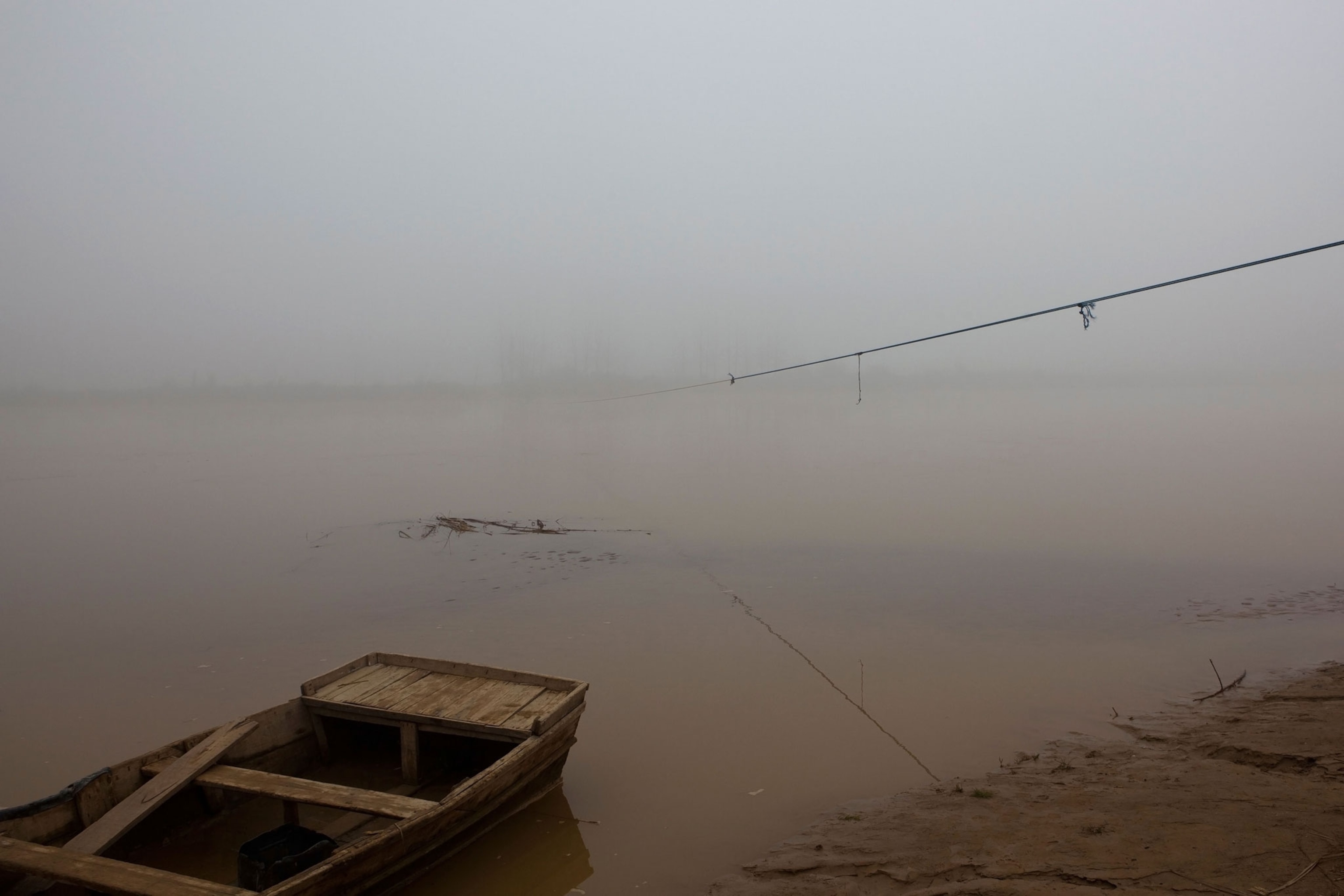 a boat on the shore of a foggy and calm river
