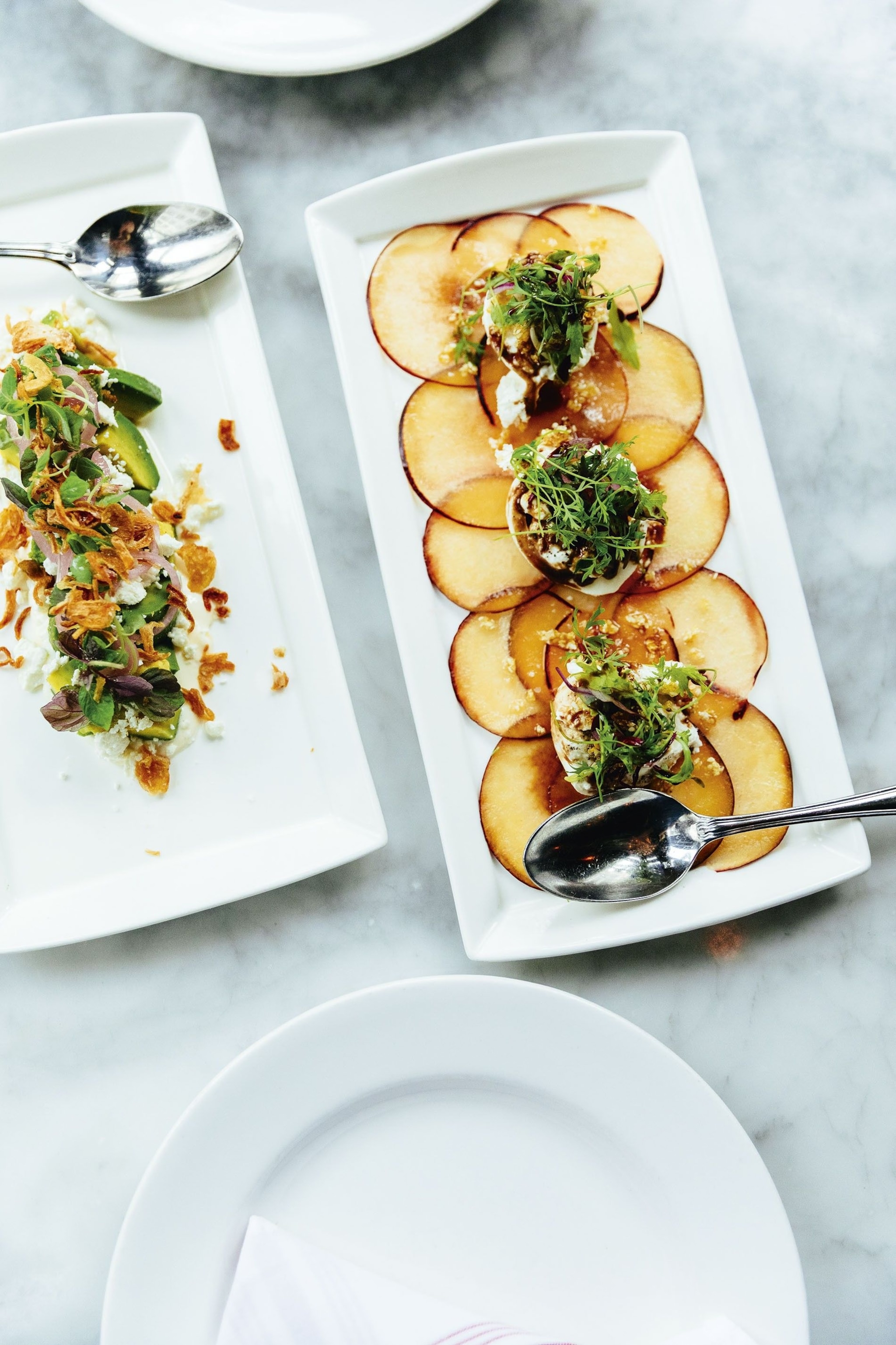 Avocado salad with feta and crispy shallots next to a burrata cheese plate with stone fruit, Wright & Company.