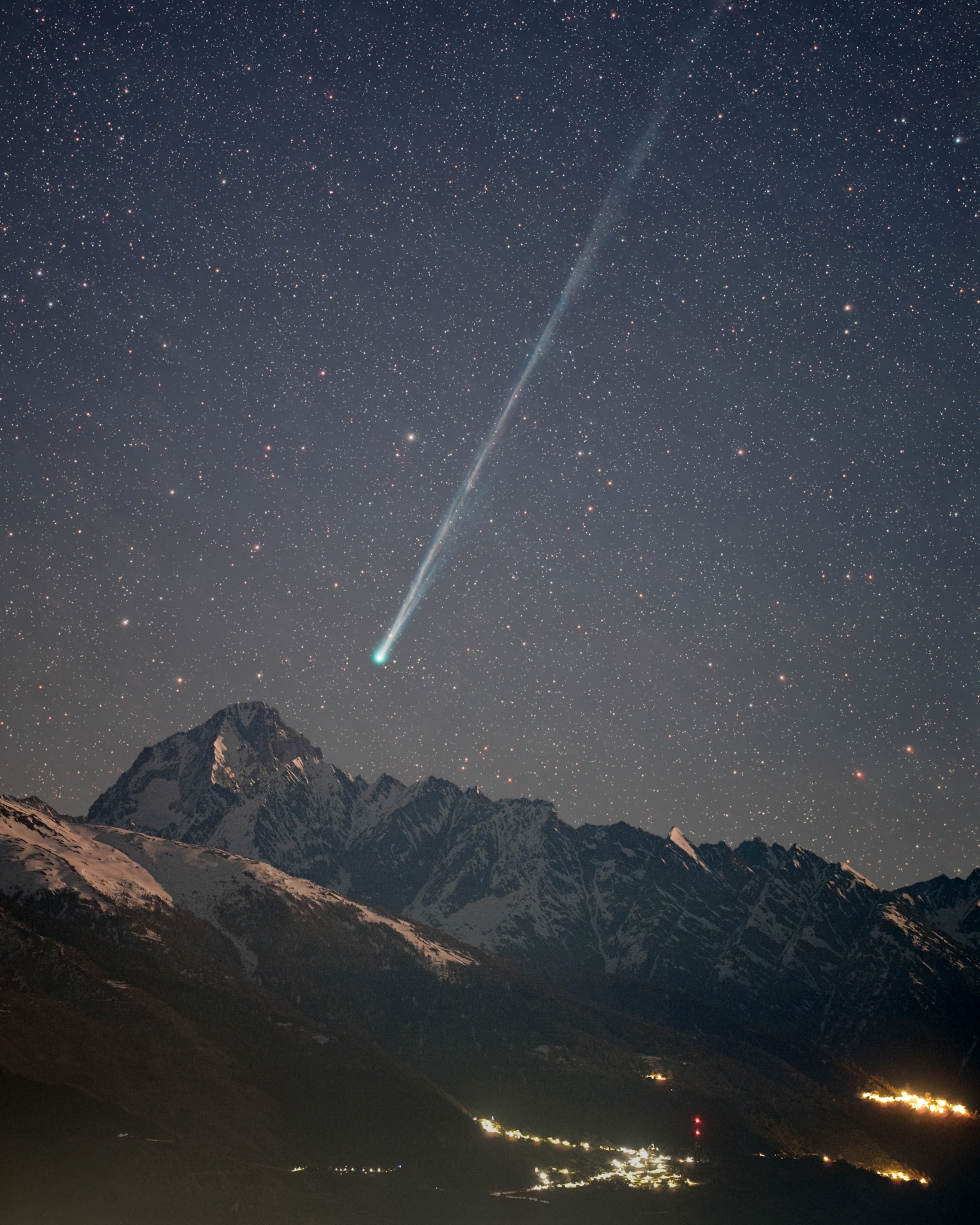 A bright comet streaks across a starry night sky over snow-capped mountains.