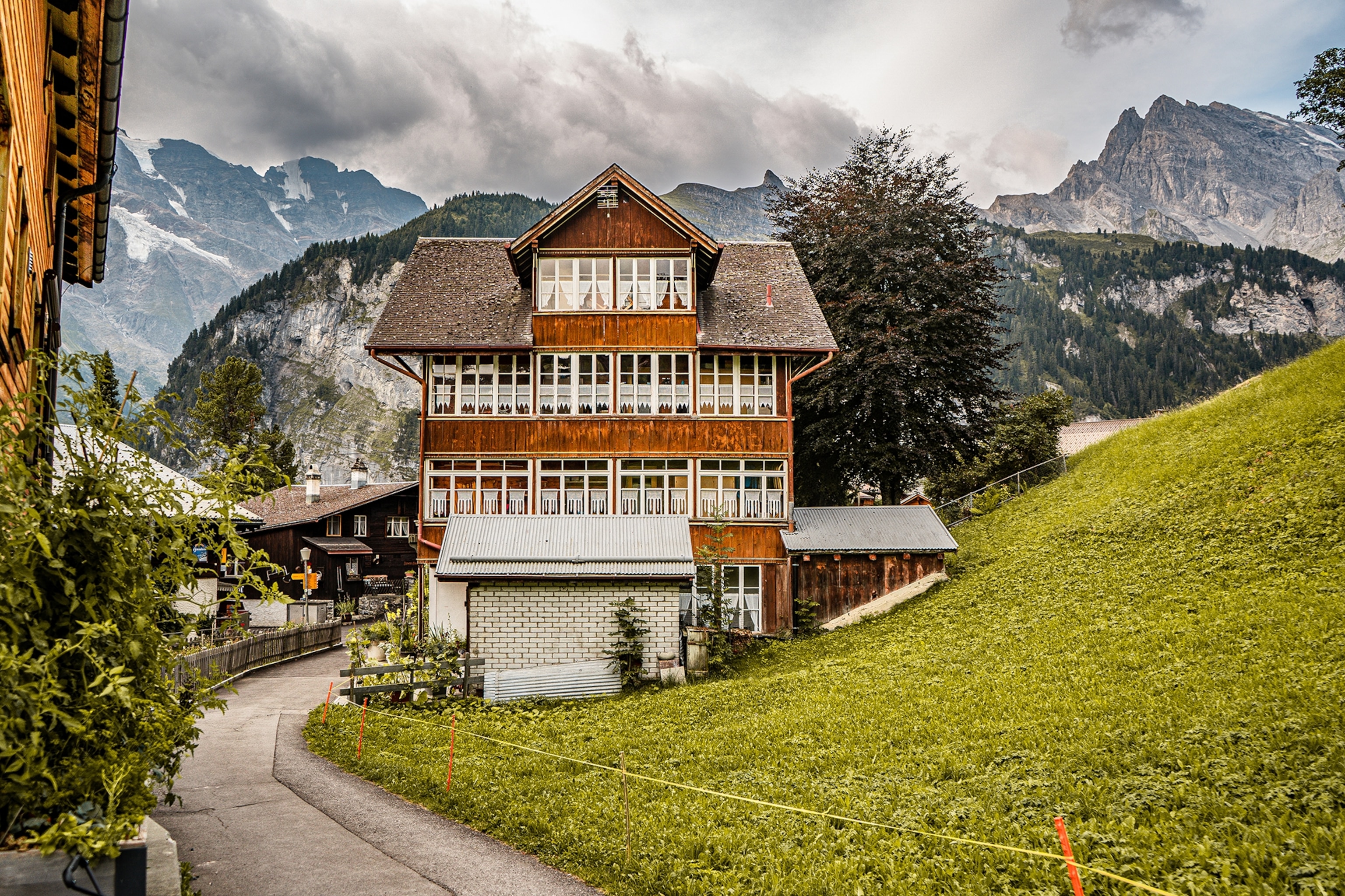 A wooden house sits on a grassy hill in the car-free mountain town of Gimmelwald.