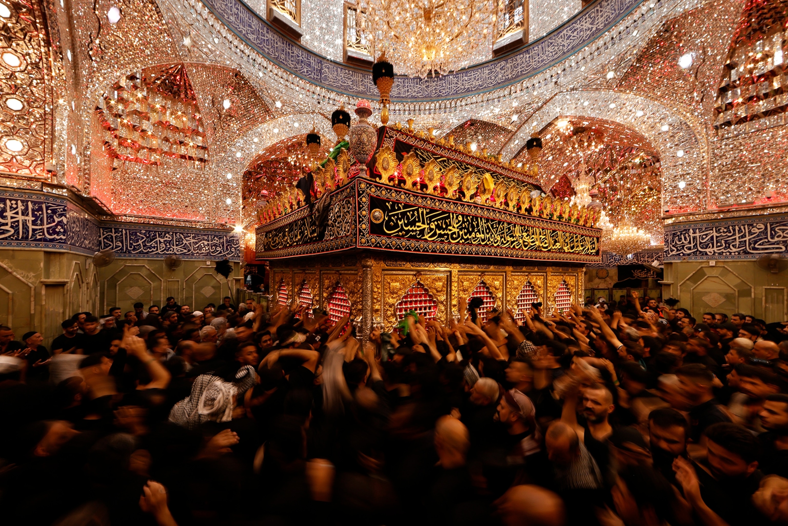A crowd of people reach their hands toward a gilded tomb
