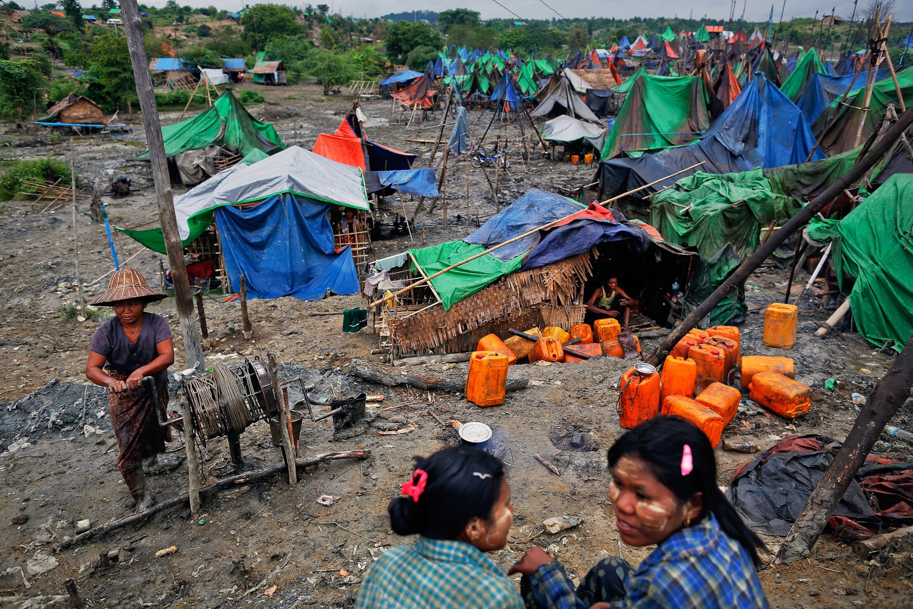 a woman manually extracting oil from a small well as girls chat at an oil field in the Minhla township of the Magwe in Myanmar.